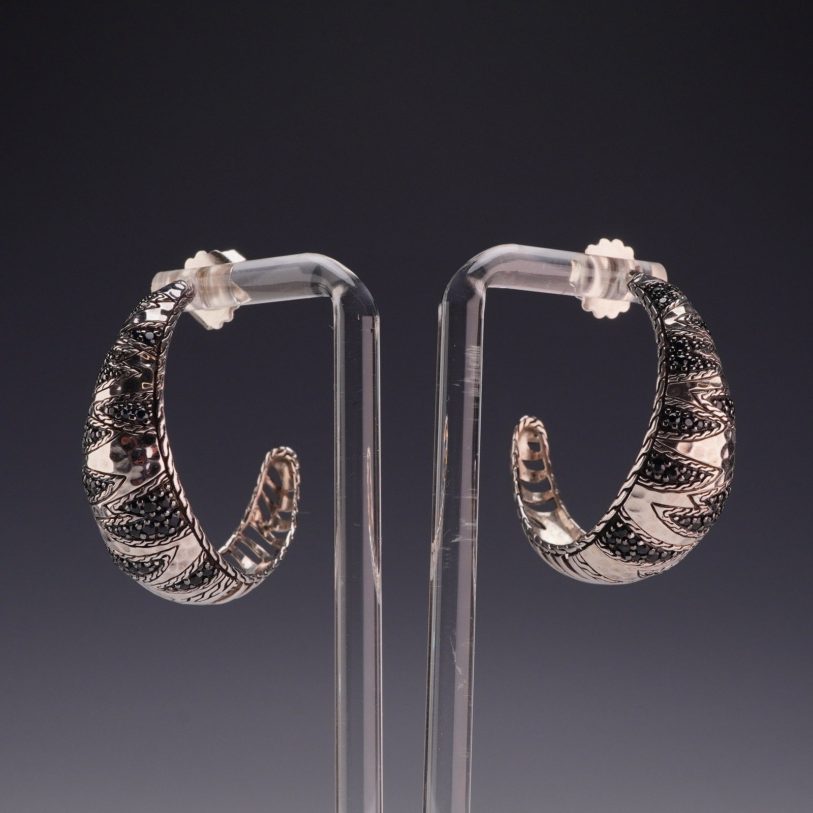 Pair of John Hardy Sterling Silver and Black Sapphire Tapered Hoop Earrings: A matched pair of John Hardy tapered C-hoop earrings crafted from sterling silver and set with black sapphires. Each earring features multiple rows of small, round-cut black sapphires in pave settings