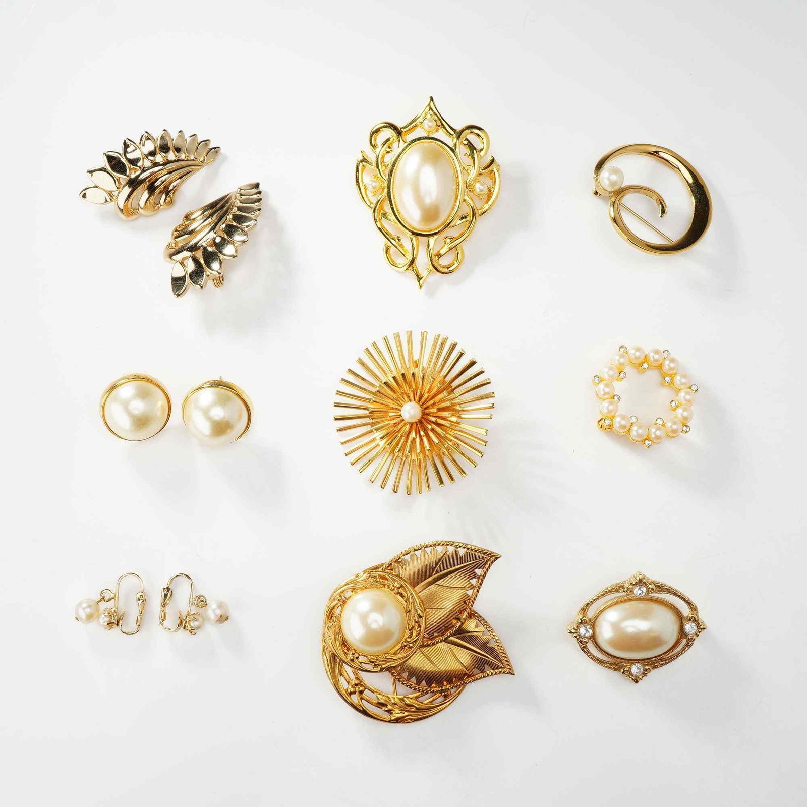 Lot of Nine Custom Jewelry: Gold Tone Brooches and Pairs of Earrings including Monet: A collection of costume jewelry featuring six brooches and three pairs of earrings, primarily constructed from gold-tone metal and accented with faux pearls and clear rhinestones. One pair of clip-on 