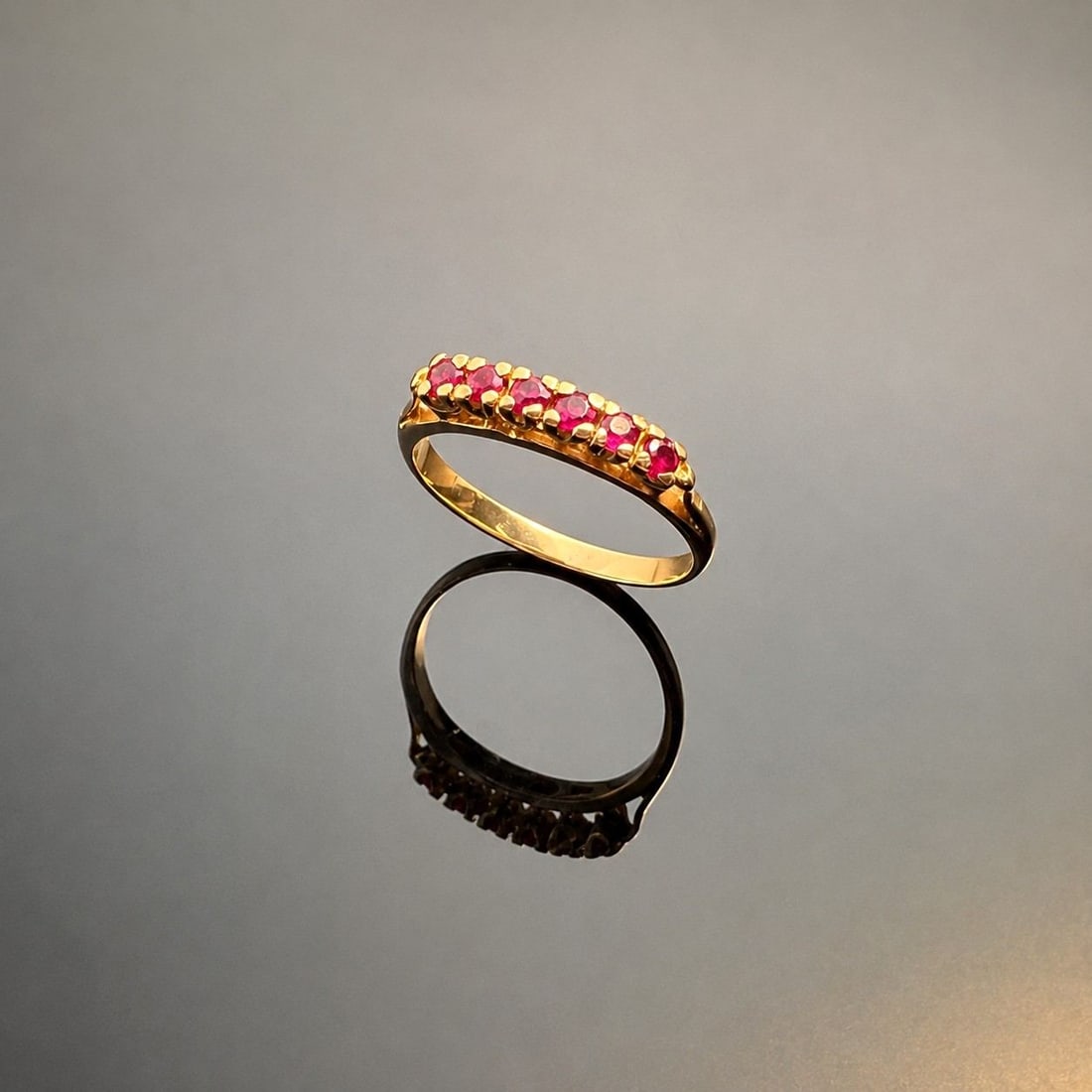 18K Yellow Gold and Ruby Ring: Crafted from 18K yellow gold, this band features six round pinkish-red rubies, prong set in a row. Tested with Thermo Scientific Niton XL2 XRF Precious Metal Analyzer and Presidium Gem Tester II. Dime