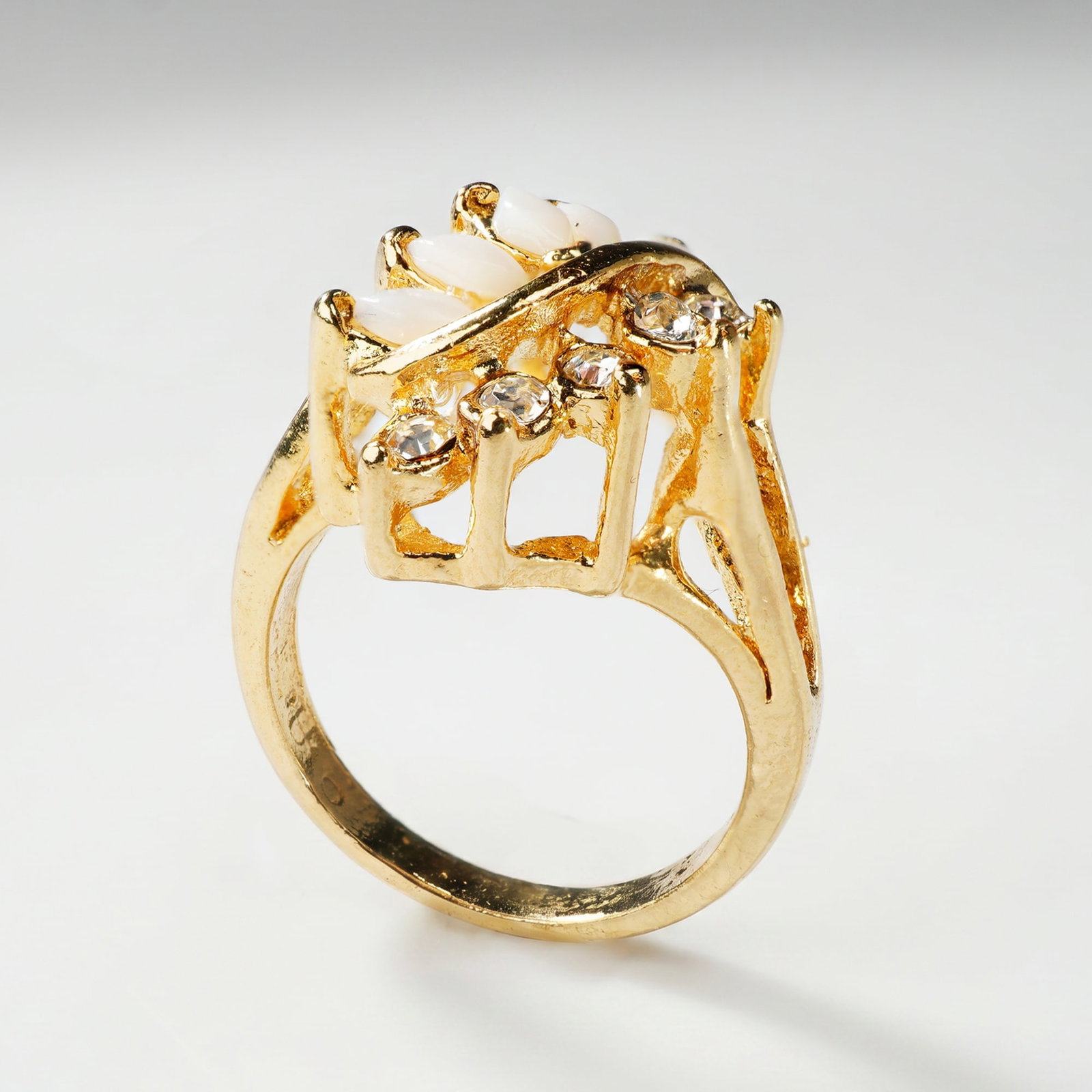 Gold Plated Faux Opal and Clear Glass Cocktail Ring: A gold-plated fashion cocktail ring featuring an asymmetrical cluster of simulated stones. The setting is composed of several marquise-cut white glass stones designed to resemble opals, paired with ro