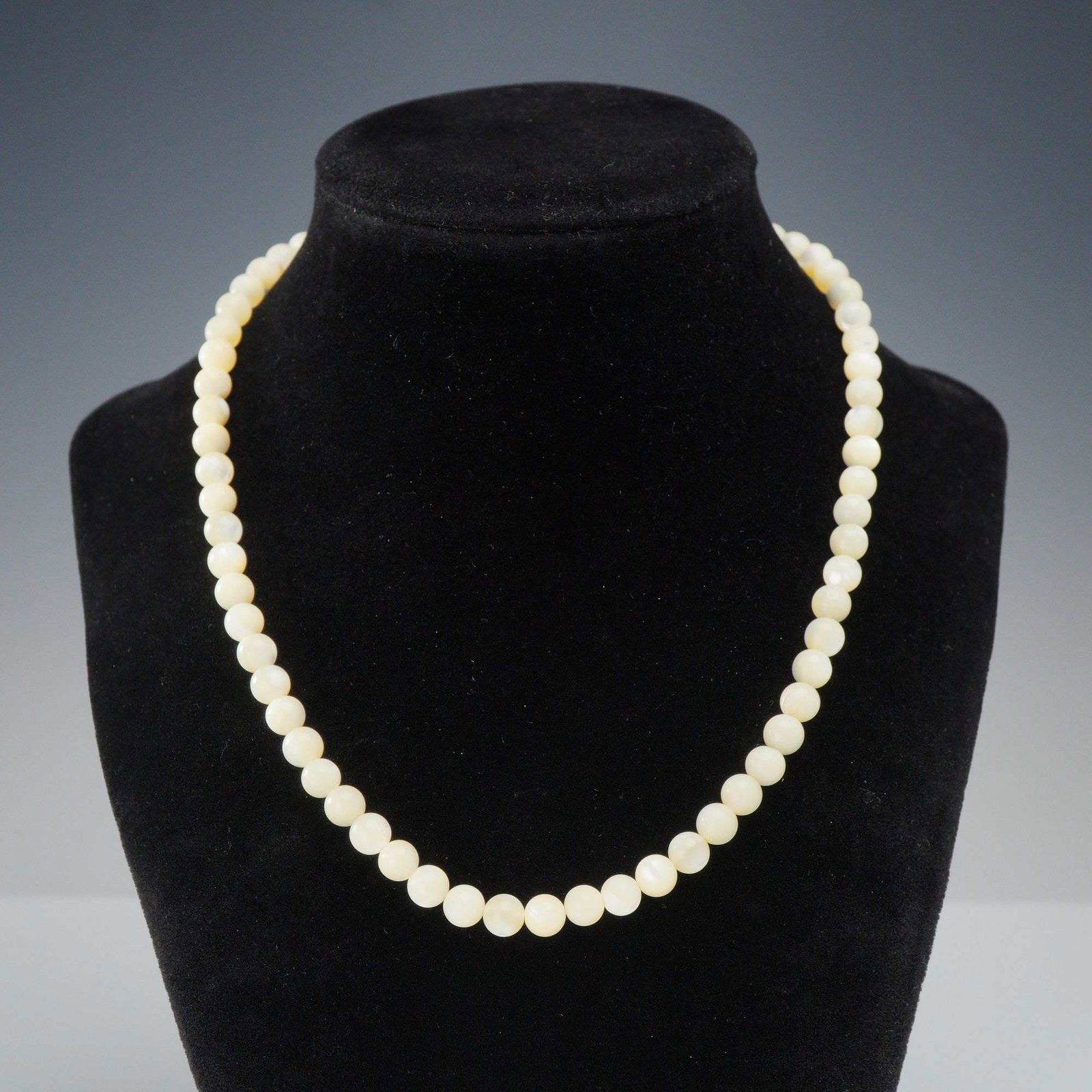 Beaded Cream Stone Necklace with Sterling Silver Filigree Clasp: A single-strand necklace composed of graduated round beads in a creamy-white to pale yellow hue. The material of the beads exhibits a soft luster and semi-translucent quality characteristic of angel s