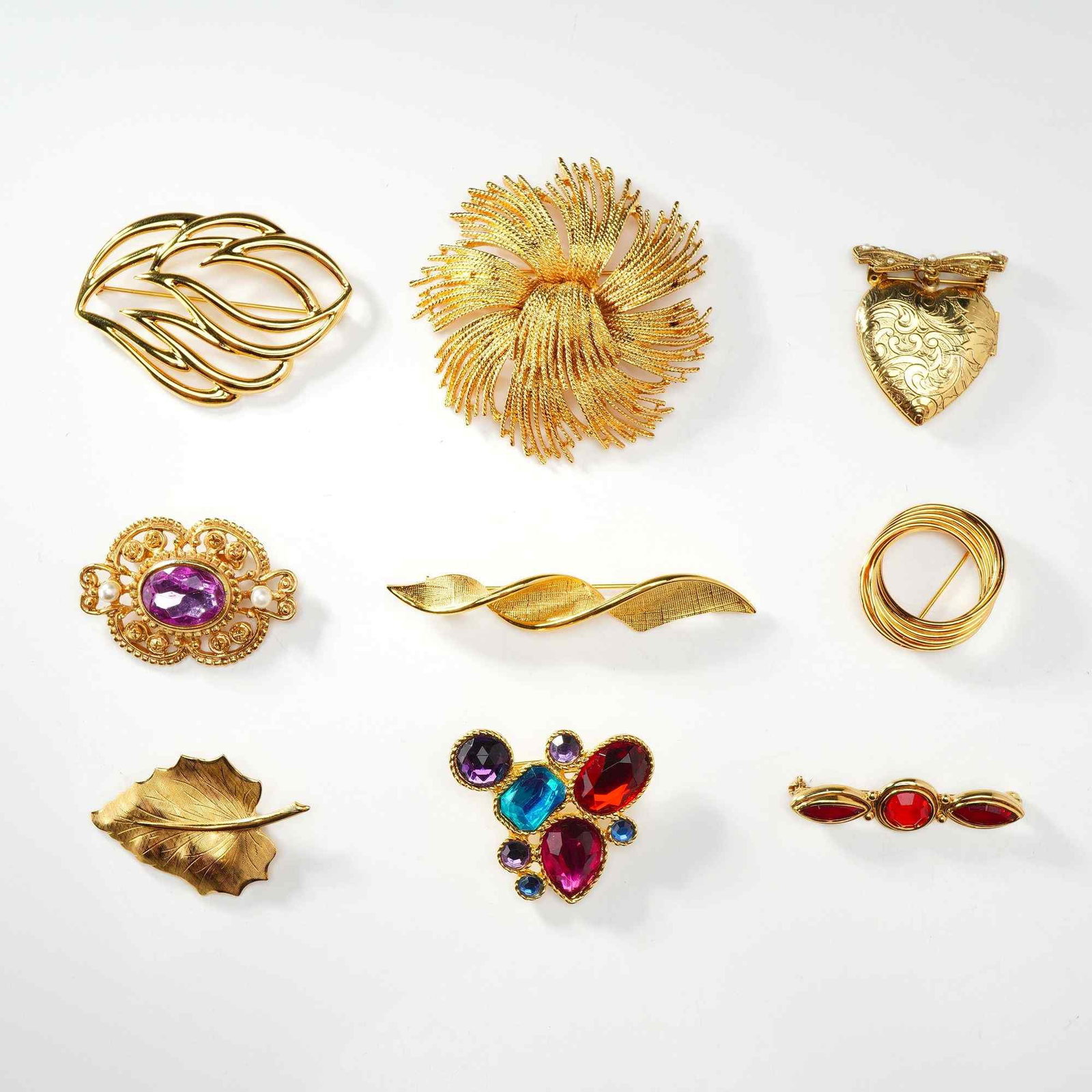 Collection of Nine Vintage Gold Tone Costume Jewelry Brooches Including Monet: An assortment of nine vintage costume jewelry brooches in various motifs. The collection features a dimensional wirework floral burst brooch marked Monet on the reverse. Other items in this 9pc group