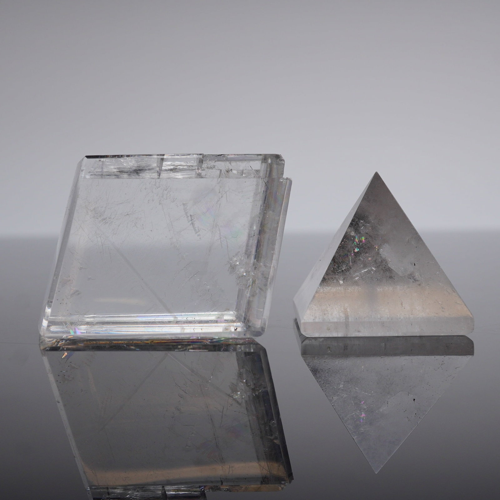 2pc Opal Calcite Prism and Quartz Pyramid Paperweights: A pair of polished mineral specimens, comprising one rectangular prism and one square-based pyramid. The prism specimen is likely optical calcite, referenced as 'Opal Calcite,' exhibiting highly