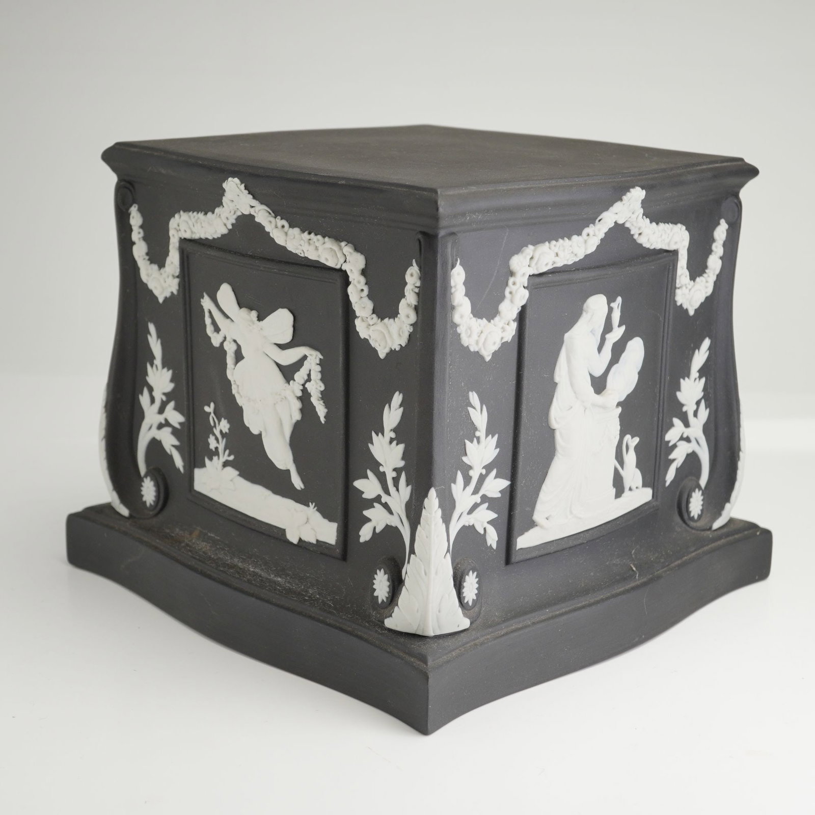 Wedgwood Black Jasperware Square Pedestal Base Plinth: A mid-to-late 20th-century Wedgwood solid black jasperware square pedestal or plinth. The object features waisted sides with scrolled corners and a flared, stepped base. Each of the four faces is deco