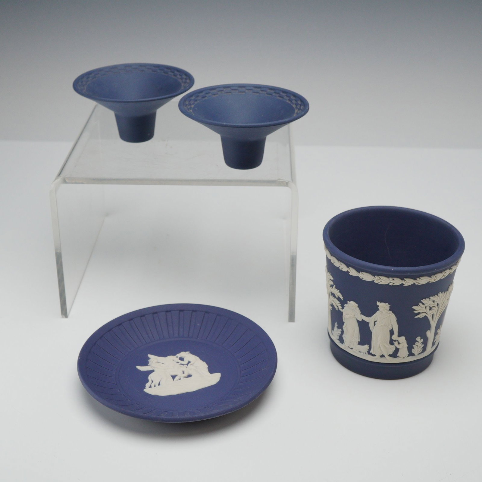 4pc Wedgwood Cobalt Blue Jasperware Lot: A group of four Wedgwood cobalt blue jasperware ceramic items featuring white sprigged bas-relief decoration. This assortment includes a small cylindrical cache pot, a miniature saucer, and a pair of 