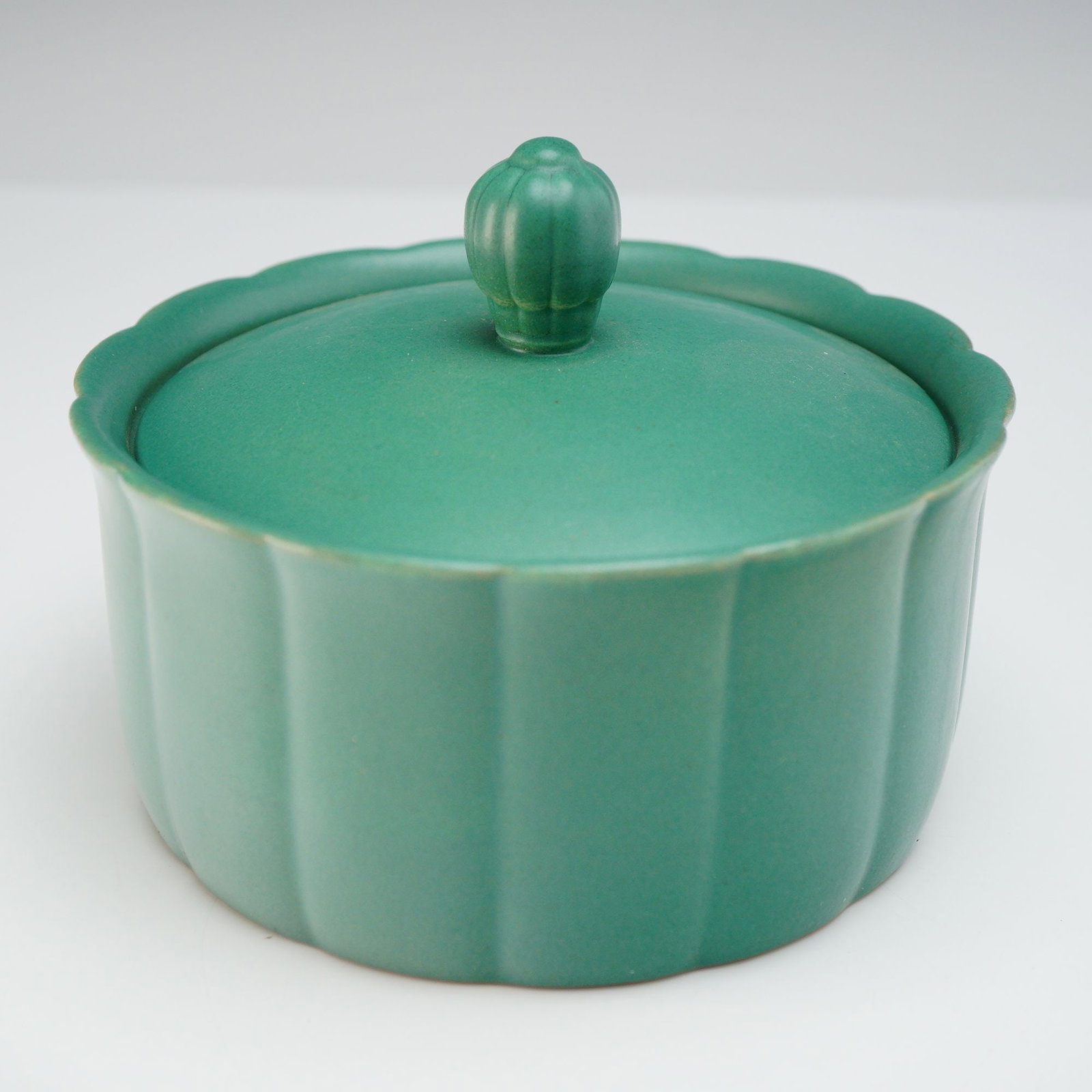 Wedgwood Green Earthenware Lidded Jar: This Wedgwood green earthenware lidded jar features a monochrome matte green glaze. The vessel is designed with a round, fluted melon-style body and a scalloped upper rim. The matching lid follows the
