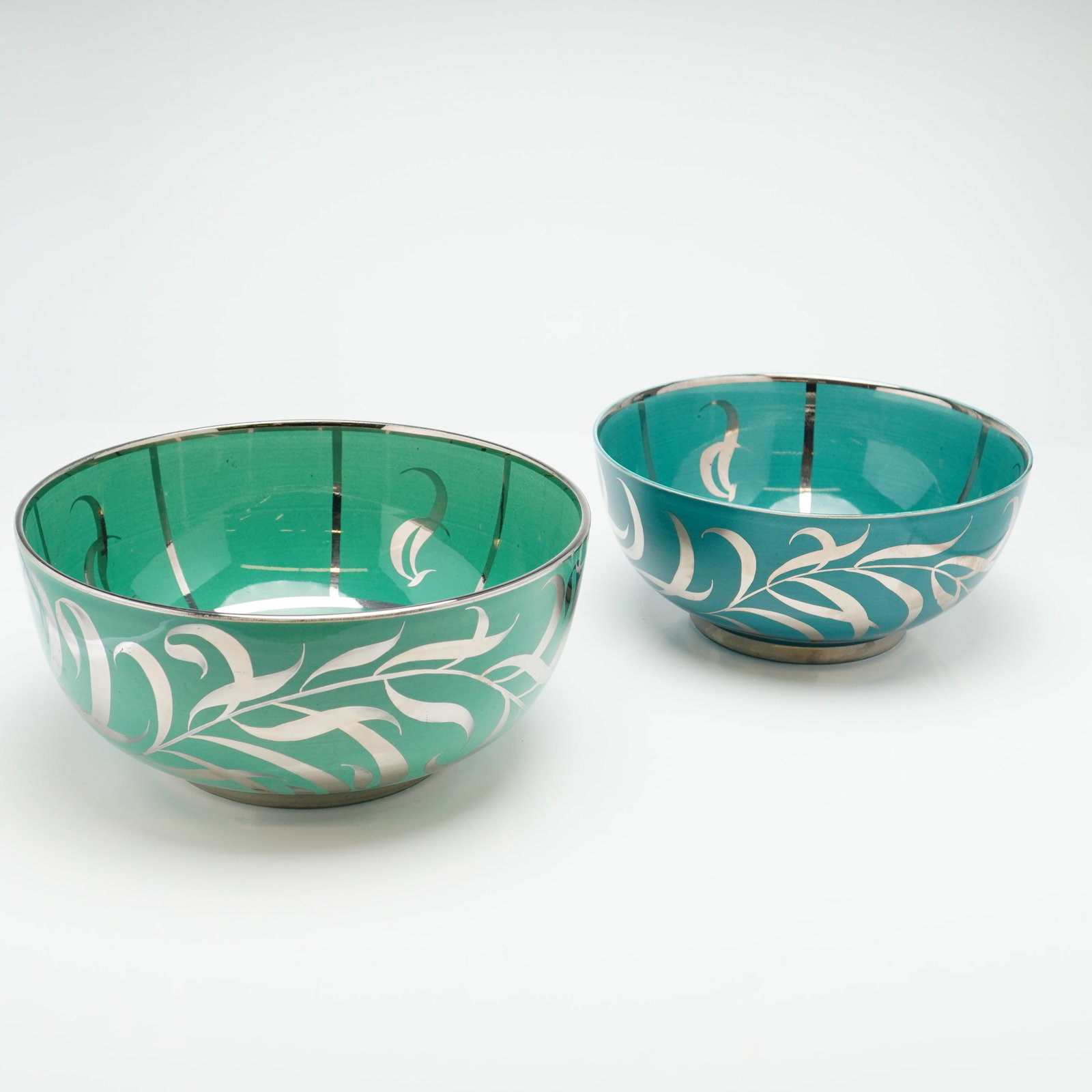 Two Wedgwood Veronese Silver Overlay Bowls: Two Wedgwood ceramic bowls featuring a turquoise glaze and silver overlay decoration. The exterior of each bowl is ornamented with a repeating foliate motif of scrolling leaves and vines in a silver-t