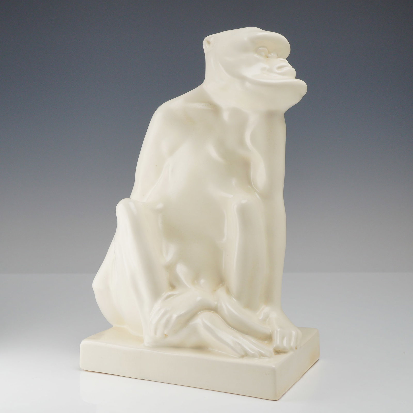 Wedgwood and Co White Glazed Figurine, Monkey c. 1960: A Wedgwood and Co. white glazed monkey figurine executed in a stylized Art Deco manner. The piece features a seated ape in a pensive posture with its head turned sharply upward and to the left. The fi
