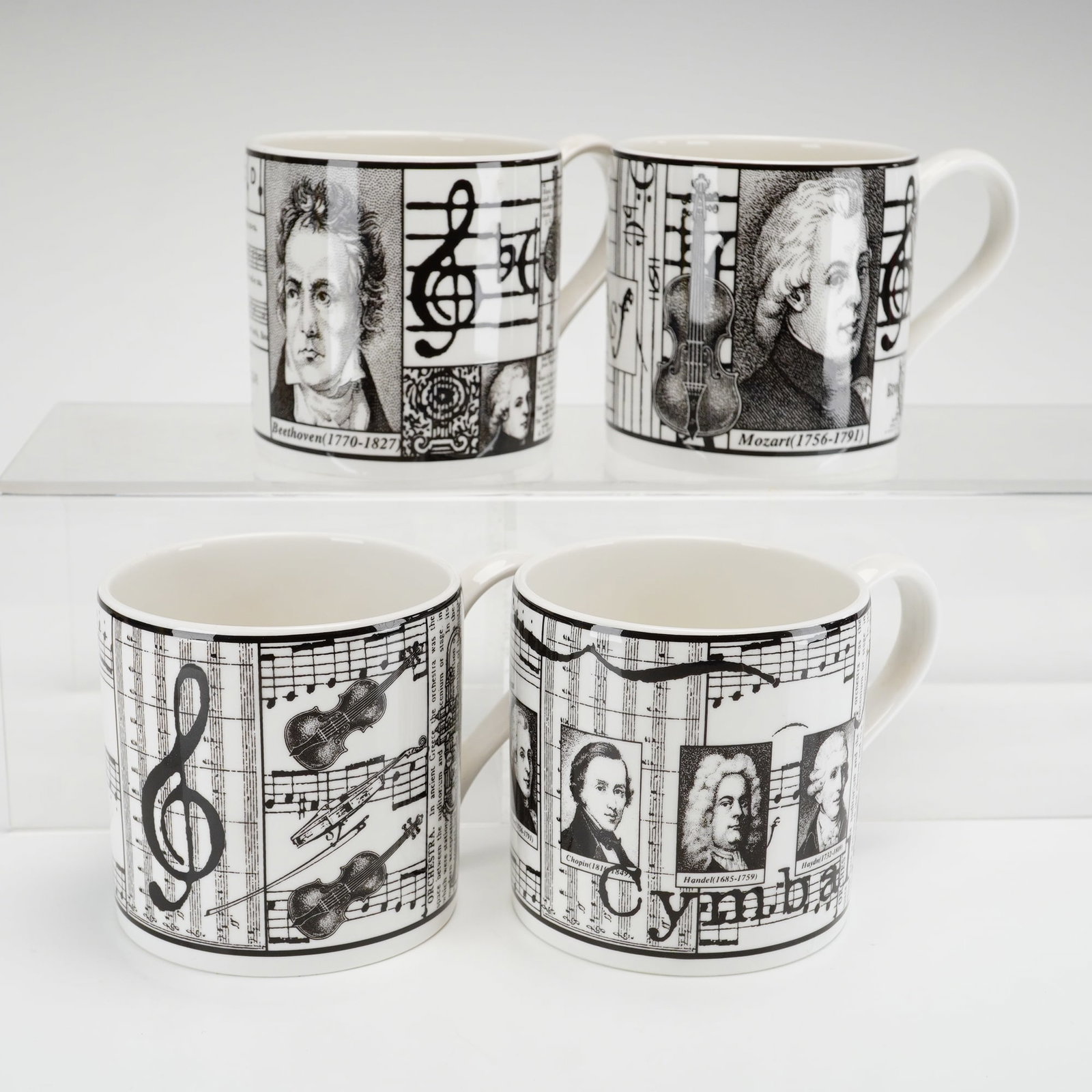 4pc Wedgwood Musical Scores Bone China Mugs: A set of four bone china mugs from the Musical Scores series by Wedgwood. Each mug features a black transfer-printed collage design on a white ground, celebrating classical music history, composers, a