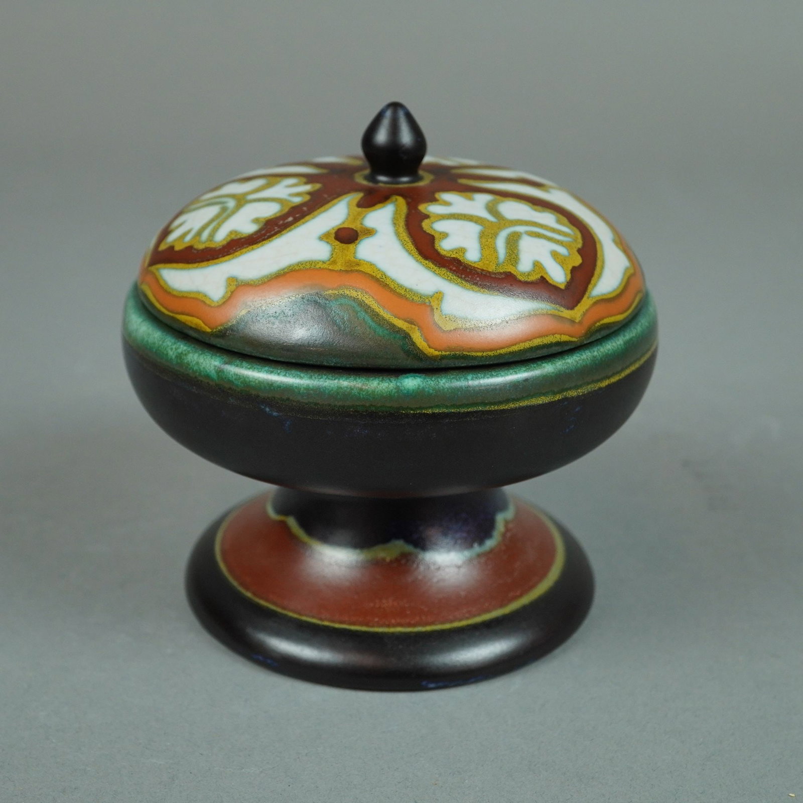 Gouda PZH Betty Pattern Lidded Box Made in Holland: A Dutch Gouda earthenware lidded box of goblet form set upon a flared pedestal base, manufactured by Plateelbakkerij Zuid-Holland (PZH). The vessel features a dark matte exterior glaze with dark purpl