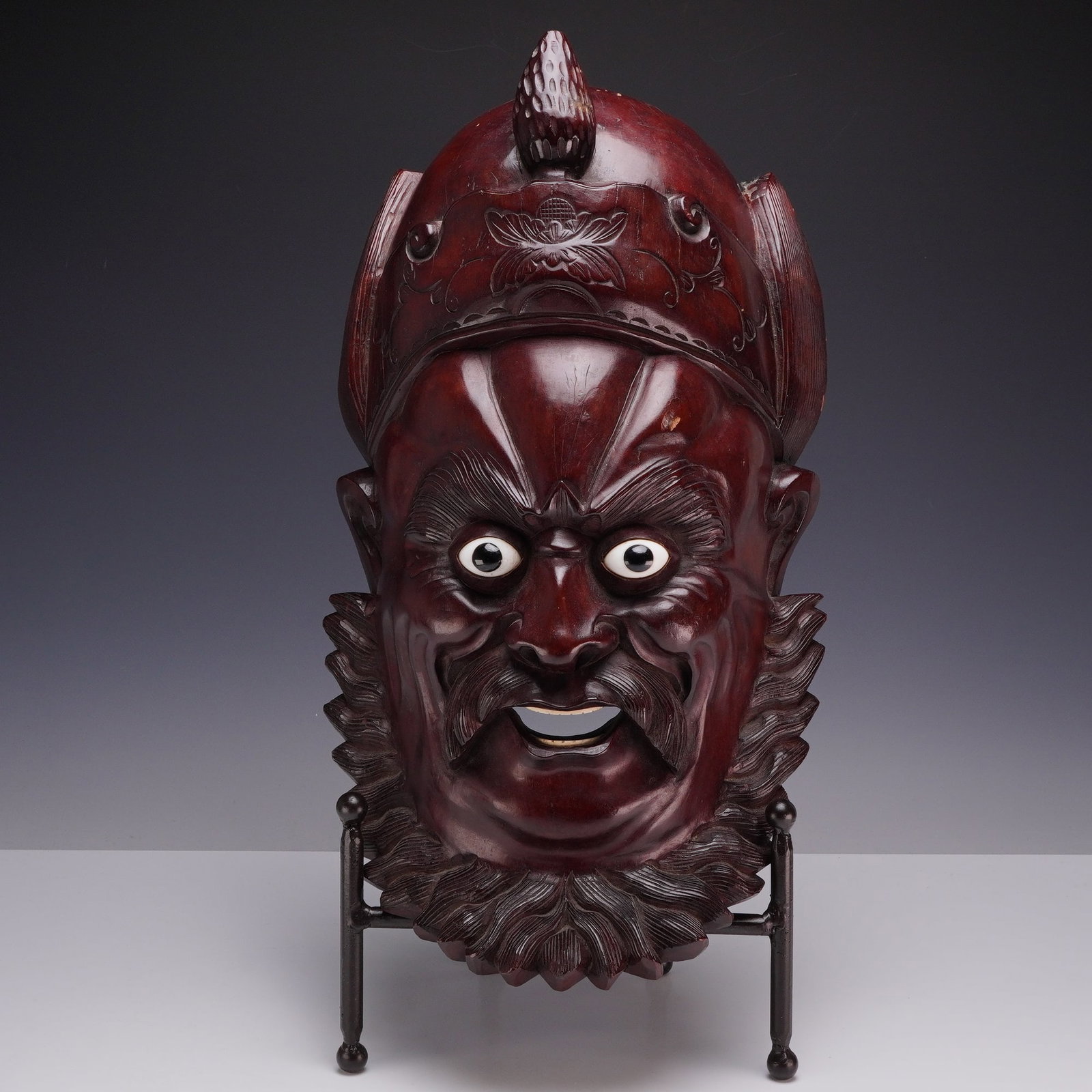 Chinese Hand Carved Rosewood Mask of a Warrior or Guardian Deity: This Chinese hand-carved mask is crafted from a dark, reddish-brown hardwood, consistent with rosewood or hongmu. It depicts a fierce character, identified in similar works as a warrior or guardian de