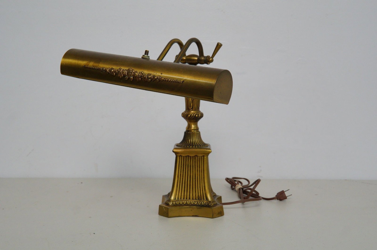 Vintage Brass Piano-Desk Lamp: Features fluted pyramid base and intricate floral details along cylindrical shade. Push button switch with florescent tube bulb. Dimensions: 12"L x 12"W x 15"H