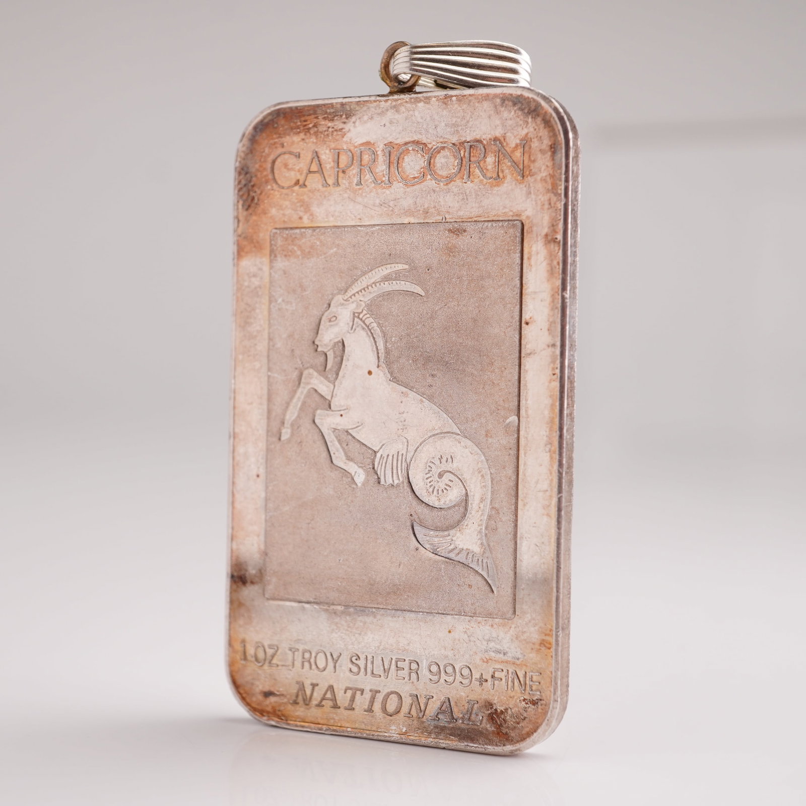 National Mint 1 Troy Oz. Silver Fine Ingot Pendent, Capricorn: .999 fine silver ingot pendant featuring a sterling silver (.925) bail. Produced by National Mint, the ingot displays a recessed relief design of Capricorn, the tenth sign of the zodiac, representing
