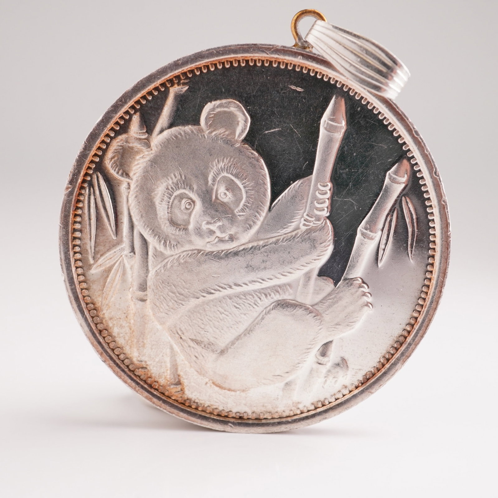 1 oz. .999 Fine Silver Round Bullion Pendent, Panda: .999 fine silver bullion round featuring a panda cub gripping a bamboo stalk on the obverse. The reverse presents a simple, unadorned field bordered by the inscription "One Ounce .999 Fine Silver"