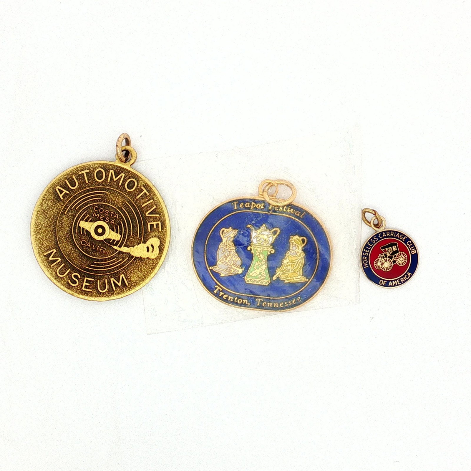 3pc Automotive and Festival Charms: A collection of gold-tone charms featuring the Horseless Carriage Club of America, the Automotive Museum in California, and the Teapot Festival in Tennessee. Dimensions: 1.25"L x 1.5"H Weight: 22.4 g
