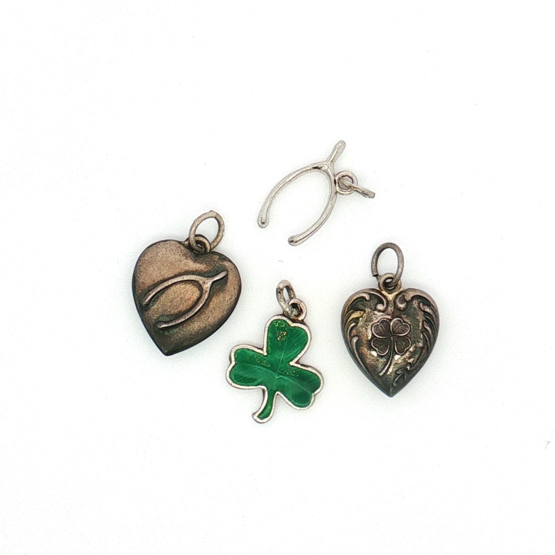4pc Sterling and Non-Sterling Silver Lukcy Charms, Clovers and Wishbones: A group of silver charms with lucky-themed designs. The lot includes two heart-shaped charms, one featuring a four-leaf clover motif and the other a wishbone motif. Also included are a wishbone charm 