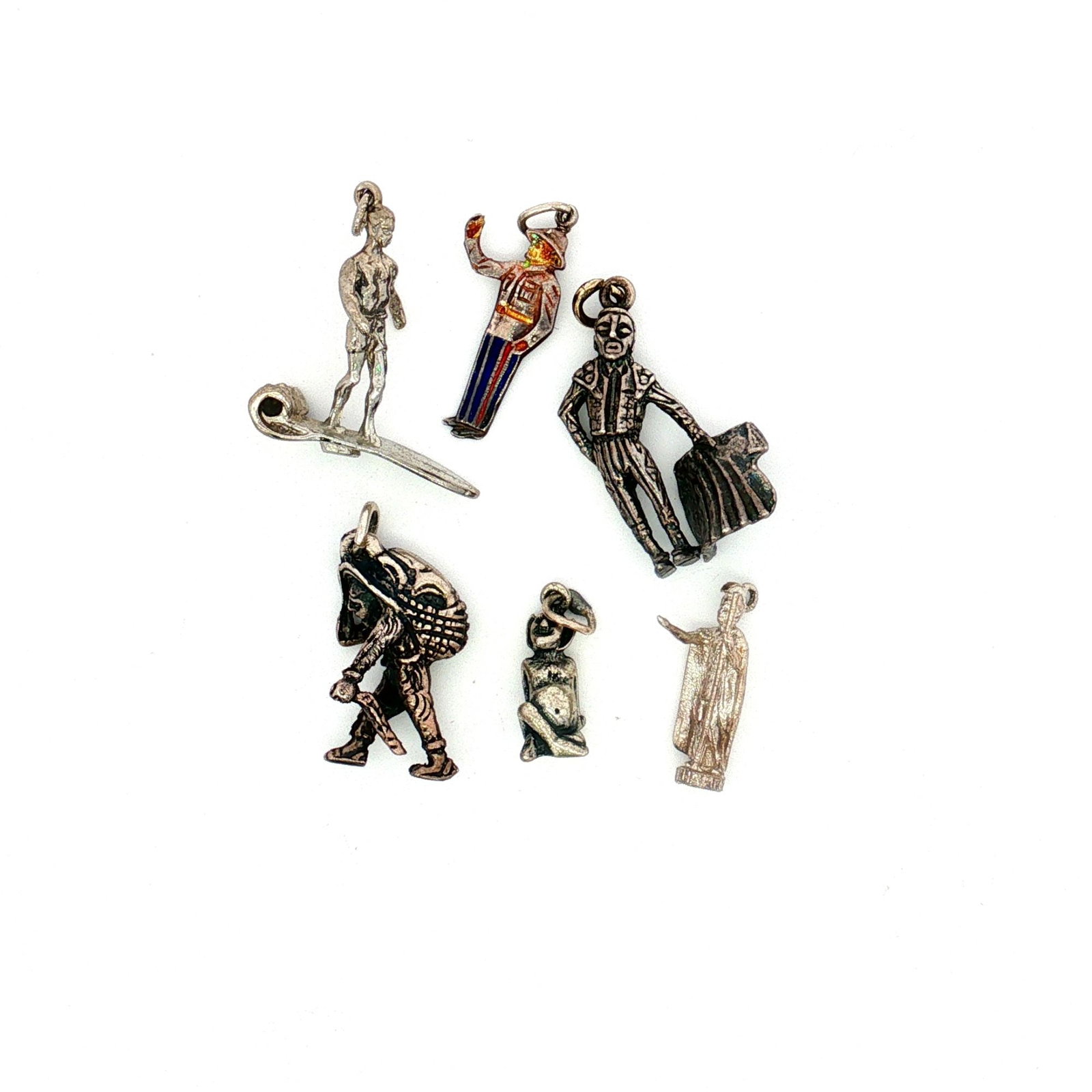 6pc Sterling and Non-Sterling Silver Figure Charms: A collection of silver charms featuring various figures including a Bahamanian police officer, King Kamehameha I, a surfer, a matador, and more. Most pieces are marked Sterling. Dimensions: 1"L x 1"H 