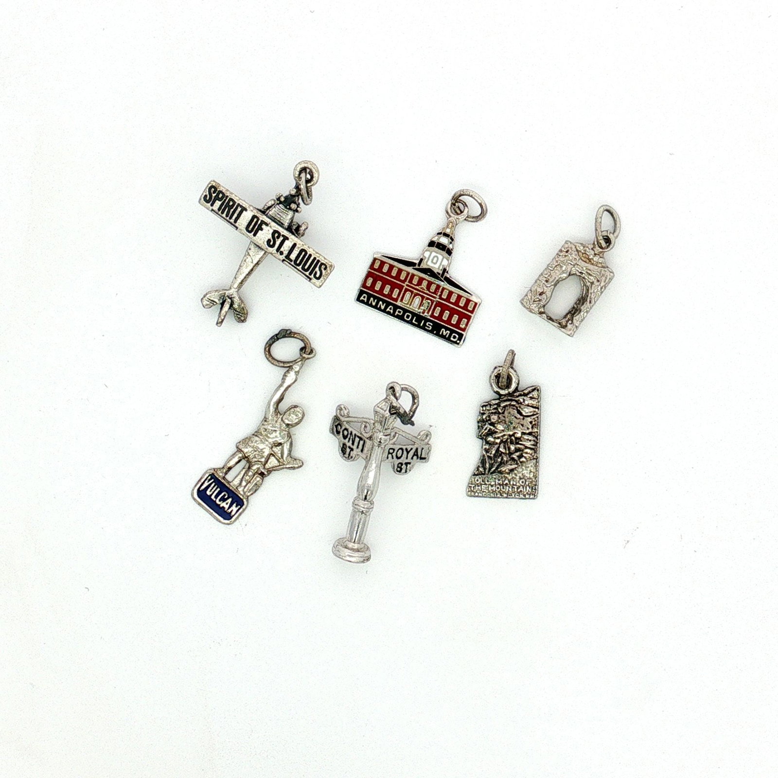 6pc Sterling and Non-Sterling Silver Miniature U.S. Landmarks and Locations Charms: A group of silver charms depicting various U.S. landmarks and locations. The set includes an enameled charm depicting the Maryland State House, a New Orleans street sign, the Old Man of the Mountain, 