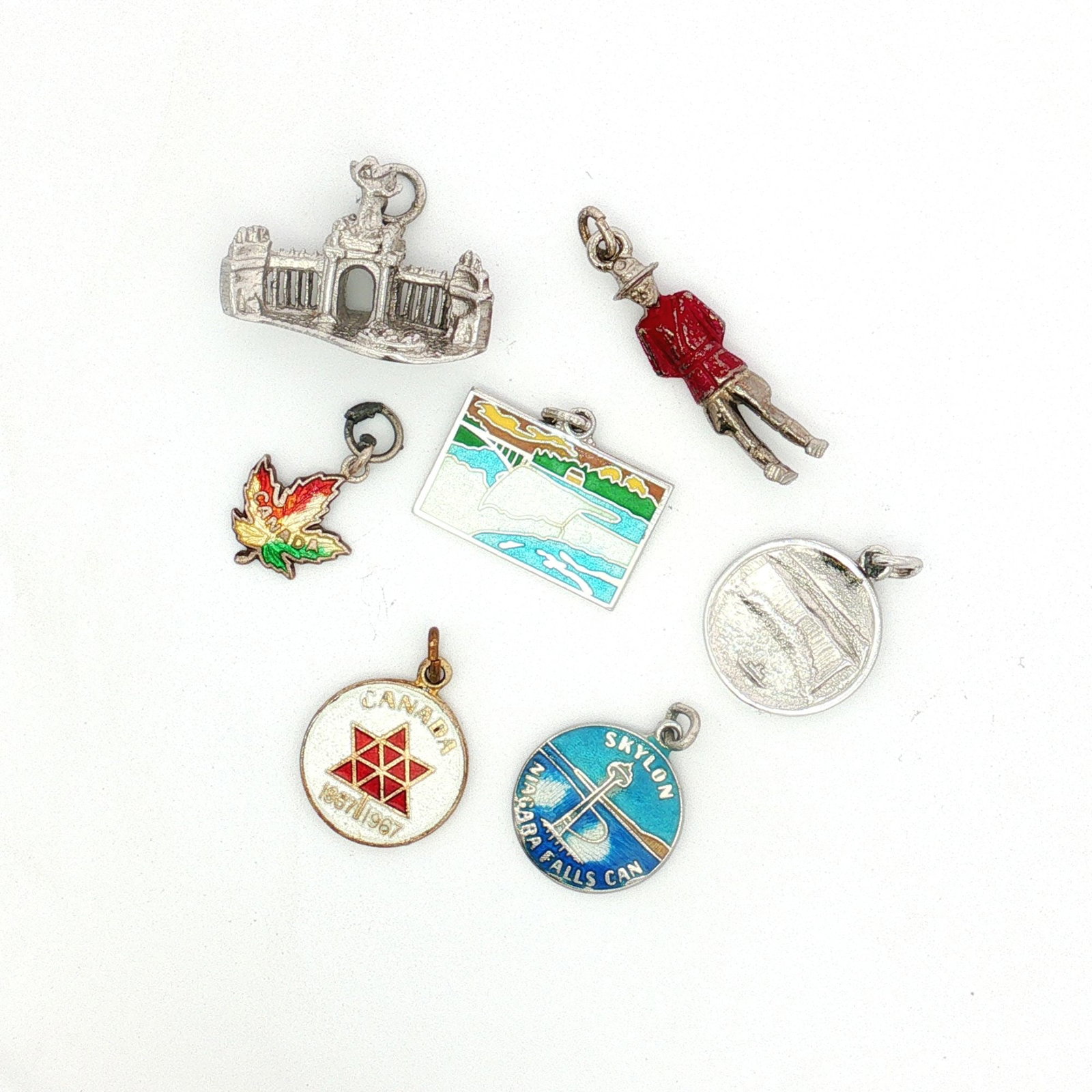 7pc Sterling and Non-Sterling Silver Canada Charms: A group of silver charms with Canada-themed designs. The lot includes two Niagara Falls charms, a charm modeled after the Princes' Gates, a charm of a Royal Canadian Mounted Police officer, a round Sk