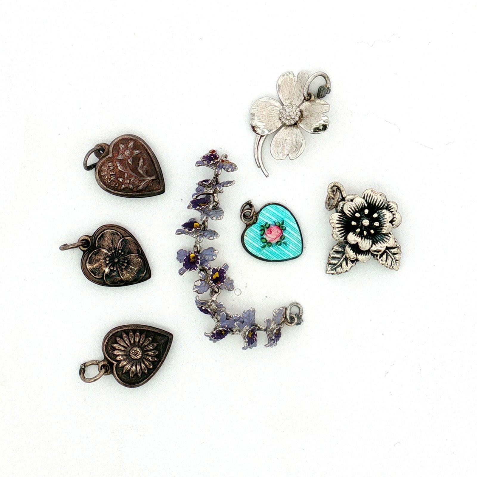 7pc Sterling Silver Flower-Themed Charms: A group of sterling silver charms with flower-themed designs. The lot includes four heart-shaped charms, each featuring a flower motif, as well as a camellia charm, a dogwood flower charm, and a link 