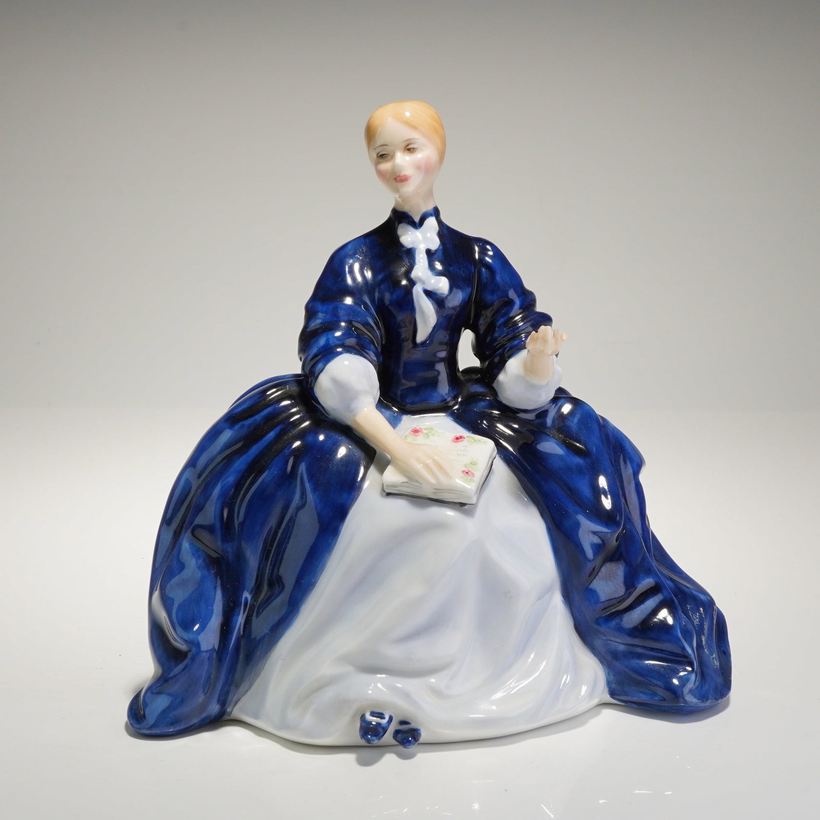 Royal Doulton Porcelain Figurine Laurianne HN2719: A glazed porcelain figurine by Royal Doulton, depicting "Laurianne," dressed in a voluminous Victorian-style gown rendered primarily in deep cobalt blue glaze and white, holding a small floral-decorat