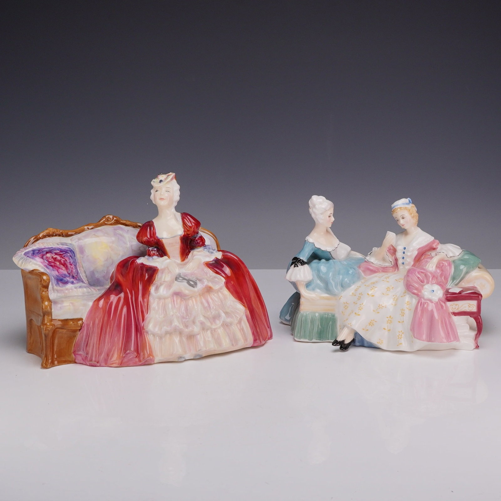 Two Royal Doulton Figurines, Belle O' The Ball HN1997 and The Love Letter HN2149: This lot consists of two Royal Doulton glazed porcelain figurines from the mid-20th century. The first piece, titled Belle O' The Ball, HN 1997, depicts a woman in a red and cream gown seated on a set