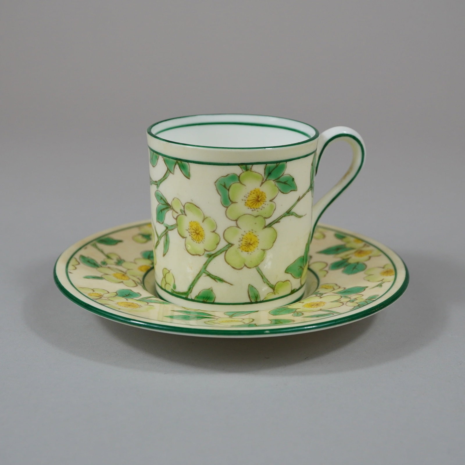 Wedgwood Bone China Hand-Painted Floral Coffee Cup and Saucer: A Wedgwood bone china coffee can and matching saucer featuring a hand-painted botanical design. The decoration consists of pale yellow flowers with orange-toned centers and green leaves set against a 