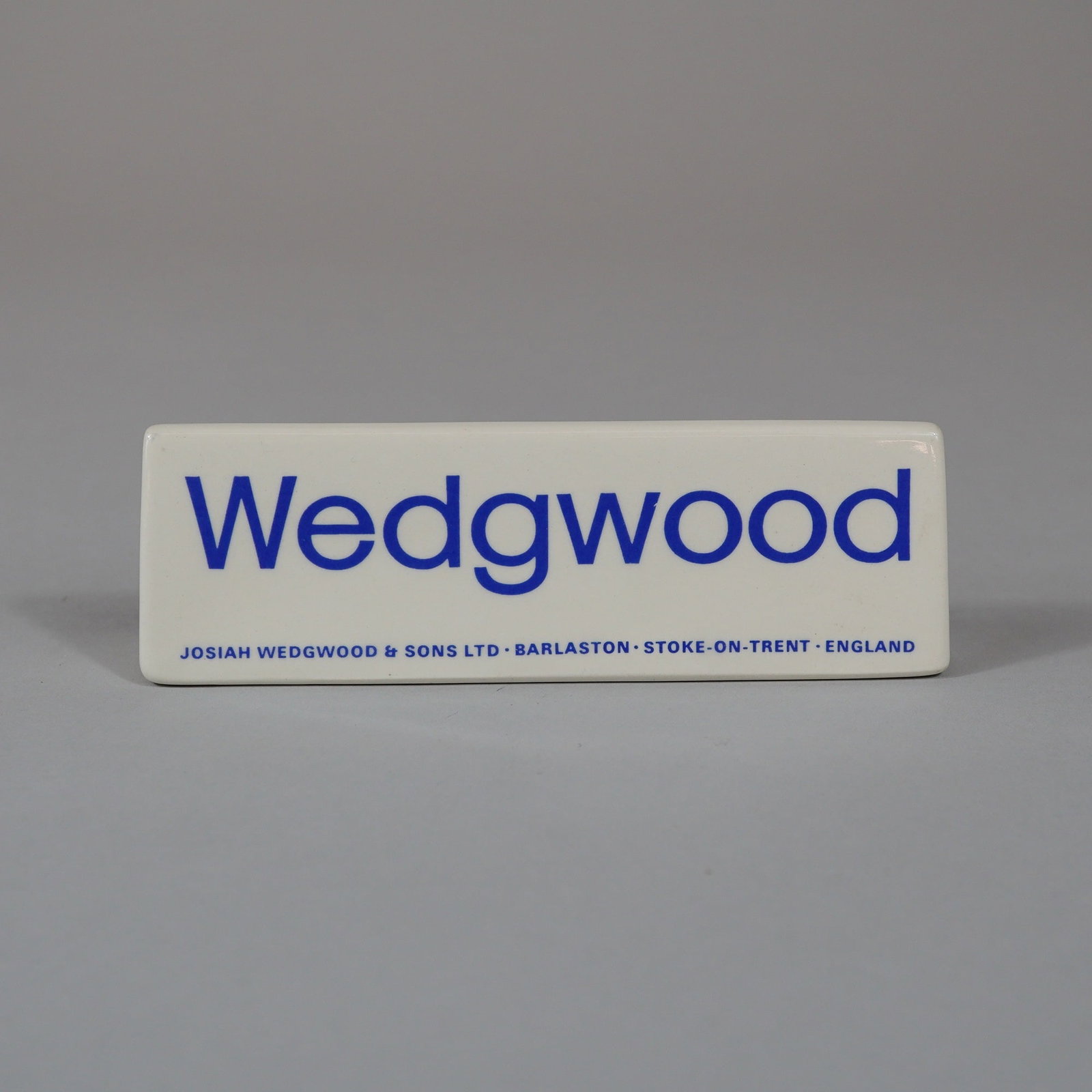 Wedgwood Ceramic Retail Advertising Display Sign: A wedge-shaped ceramic retail display sign produced by Josiah Wedgwood and Sons Ltd. The piece is constructed from white glazed ceramic and features blue transfer-printed text on the front face. The c