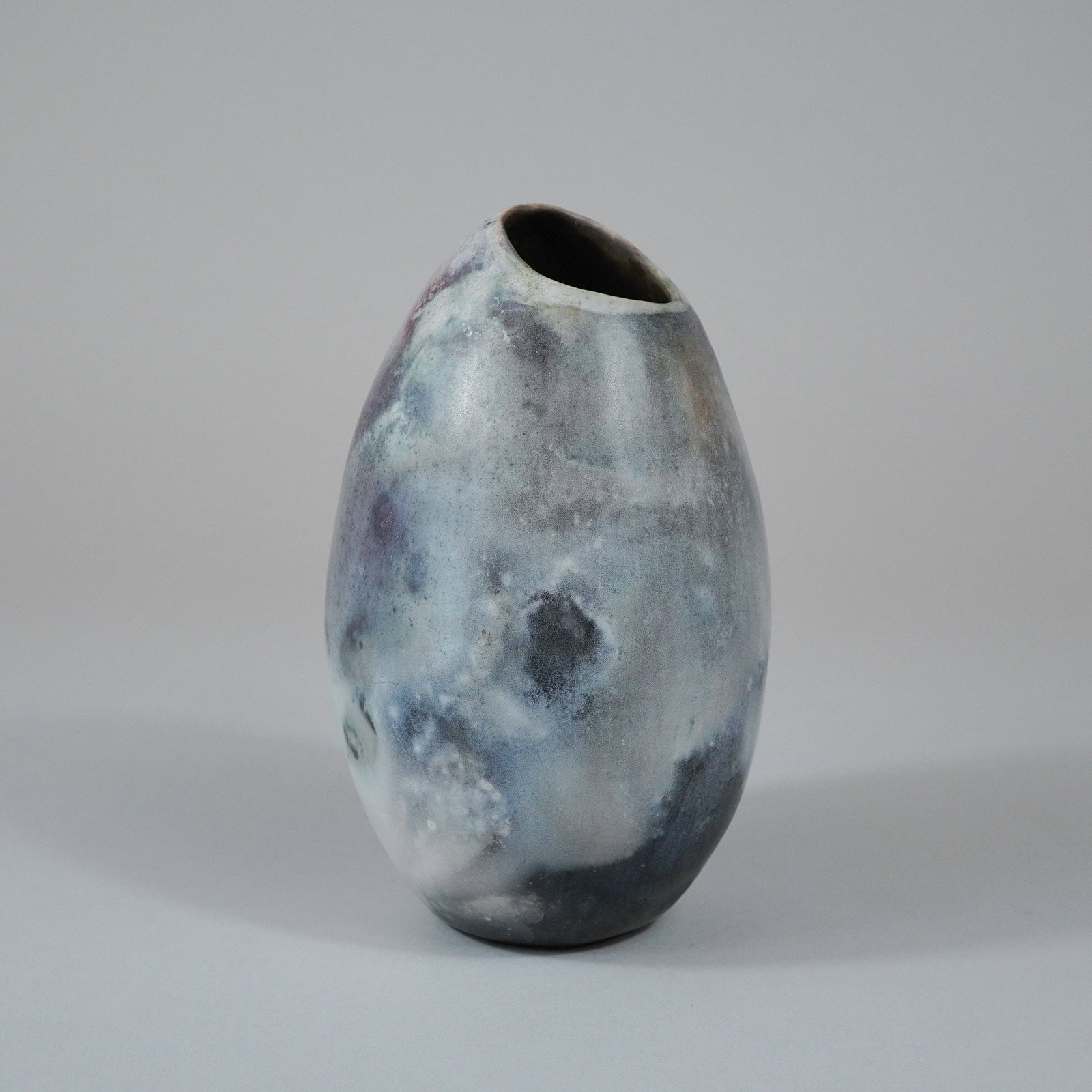 Joseph Barberio Studio Pottery Saggar Fired Stoneware Vase: A studio pottery vessel of ovoid form, crafted from stoneware and featuring an asymmetrical, slanted aperture at the top. The piece exhibits an atmospheric firing technique, likely saggar firing, resu