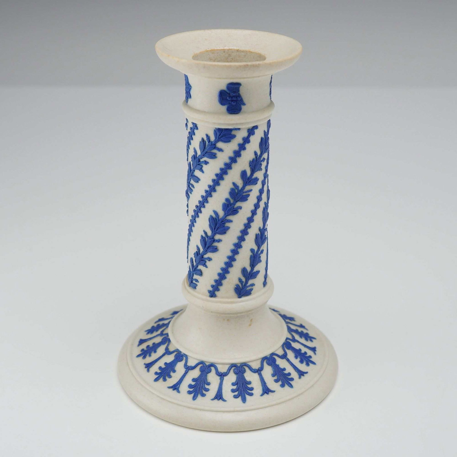 Wedgwood Blue Jasperware Candlestick: A Wedgwood white jasper stoneware candlestick featuring sprigged blue bas-relief decoration. The columnar stem is ornamented with spiraling foliate swags and beaded lines. The flared circular base dis