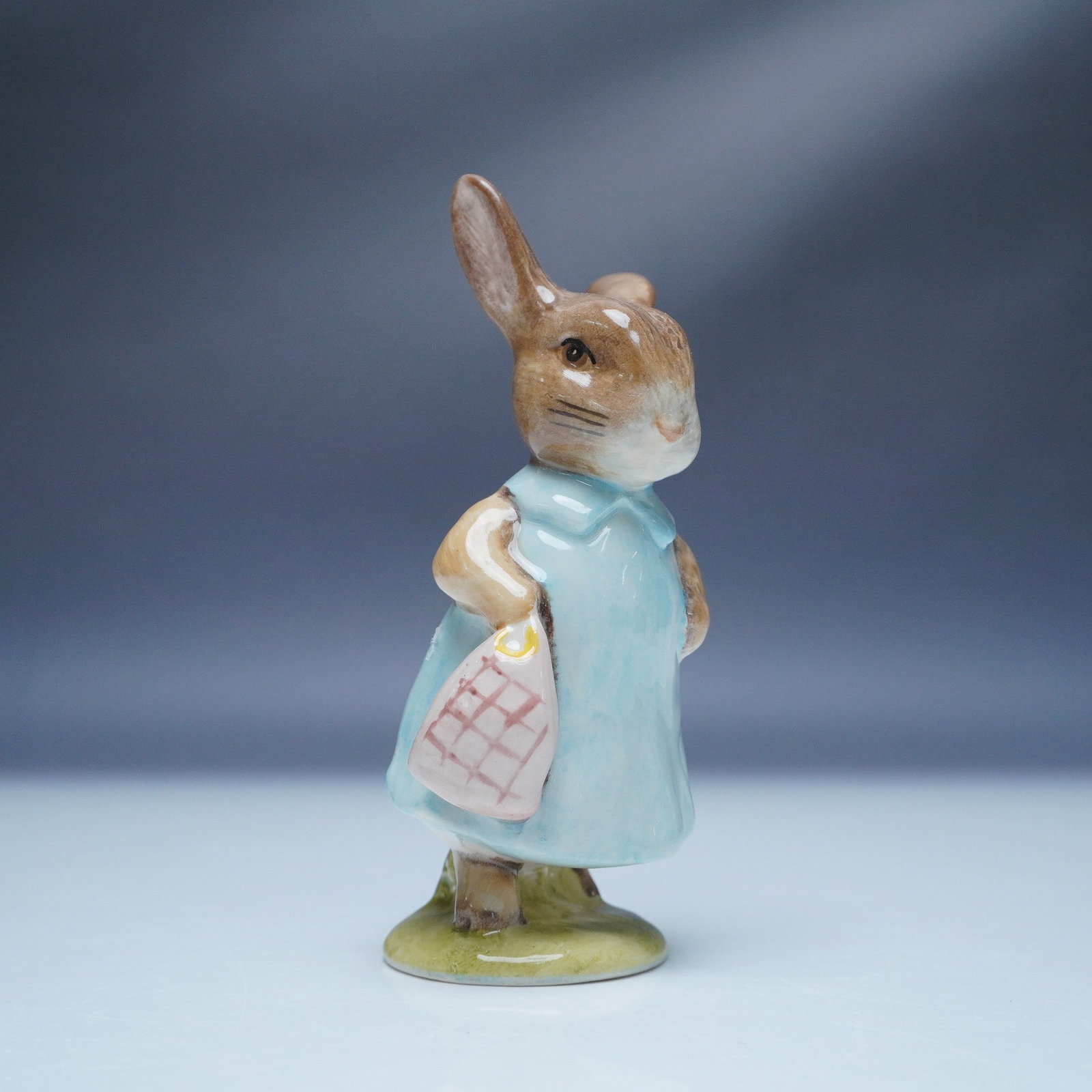 Royal Albert Beatrix Potter Figurine, Mrs Flopsy Bunny: Charming Royal Albert figurine depicting Mrs Flopsy Bunny from the beloved Beatrix Potter series. Crafted in fine bone china, this collectible features a hand painted design with delicate pastel tones