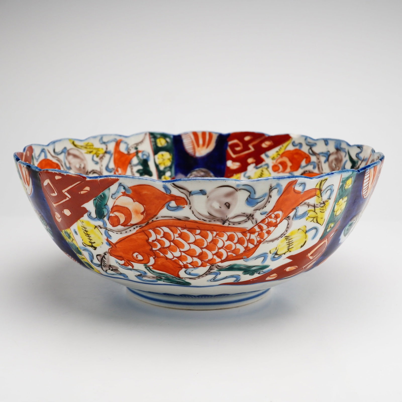 Japanese Imari Porcelain Scalloped Bowl with Carp Motif: A Japanese Imari porcelain bowl of deep circular form featuring a scalloped or foliate rim. The piece is decorated in a traditional palette using underglaze cobalt blue and overglaze iron-red, yellow,