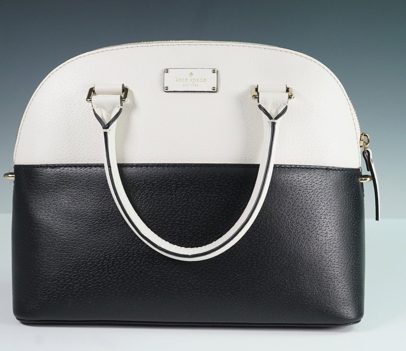 Kate Spade Black and White Dome Satchel with Gold Hardware and Strap: Kate Spade New York dome-shaped satchel crafted in pebbled leather with a bold colorblock design in black and white. The structured silhouette features dual rolled top handles and an optional, adjusta