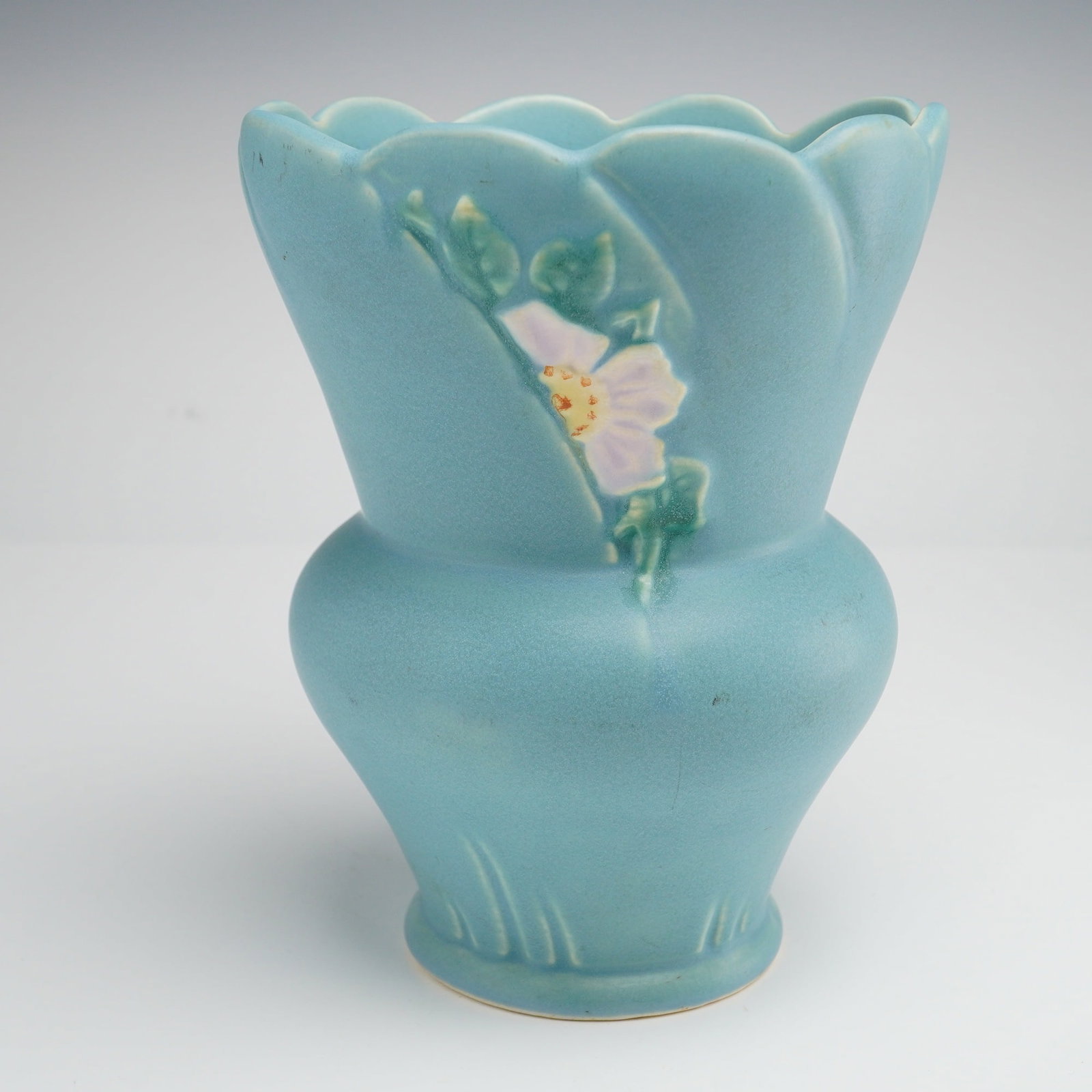 Weller Pottery Wild Rose Pattern Blue Vase: A vintage Weller Pottery earthenware art pottery vase from the 1930s Wild Rose line. This piece features a matte turquoise-blue glaze with a molded low-relief decoration of a single wild rose, hand-pa