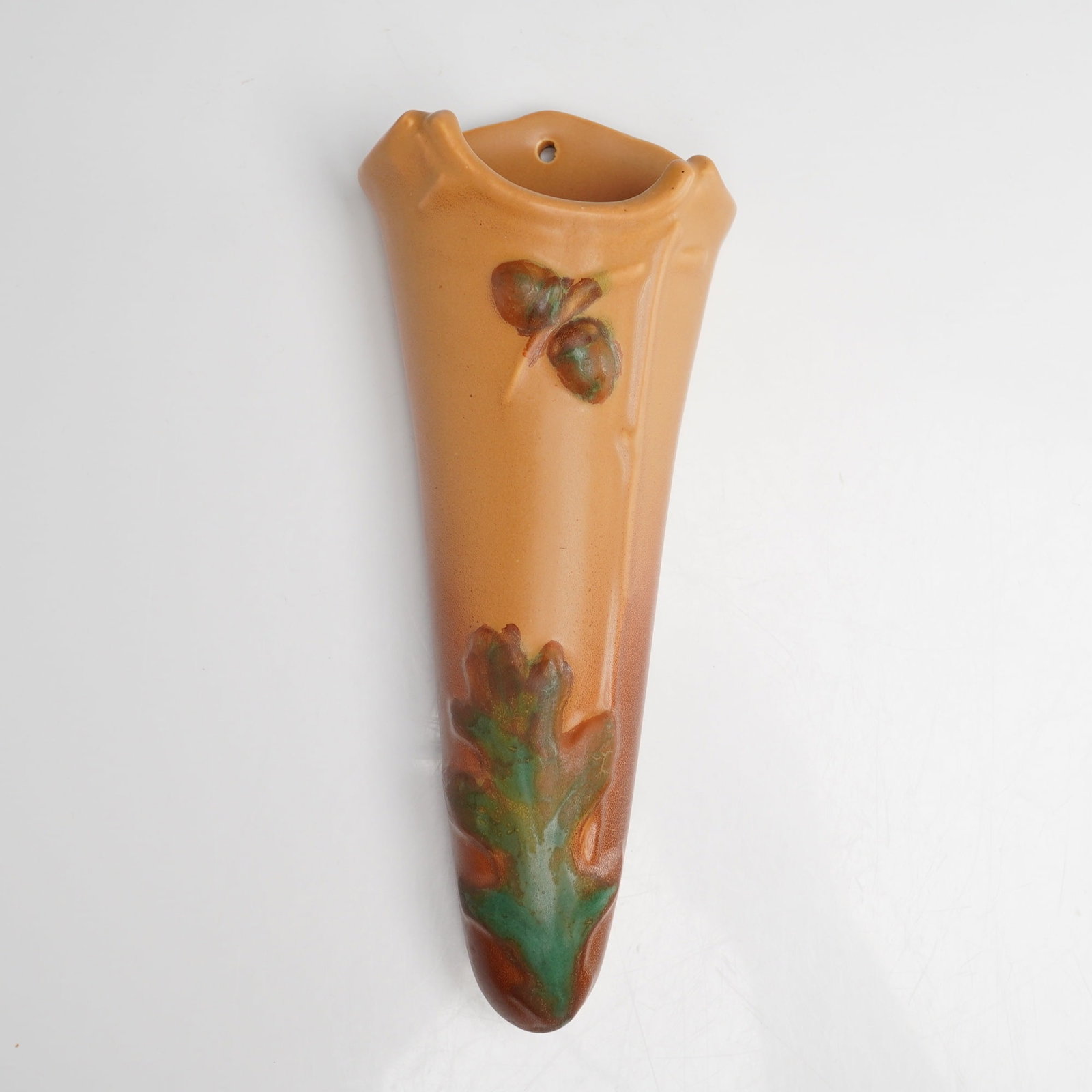 Weller Pottery Oak Leaf Wall Pocket: This American art pottery earthenware wall pocket was manufactured by Weller Pottery in the Oak Leaf pattern. The vessel features a tapered, cone-shaped form with a single mounting hole at the top. Th