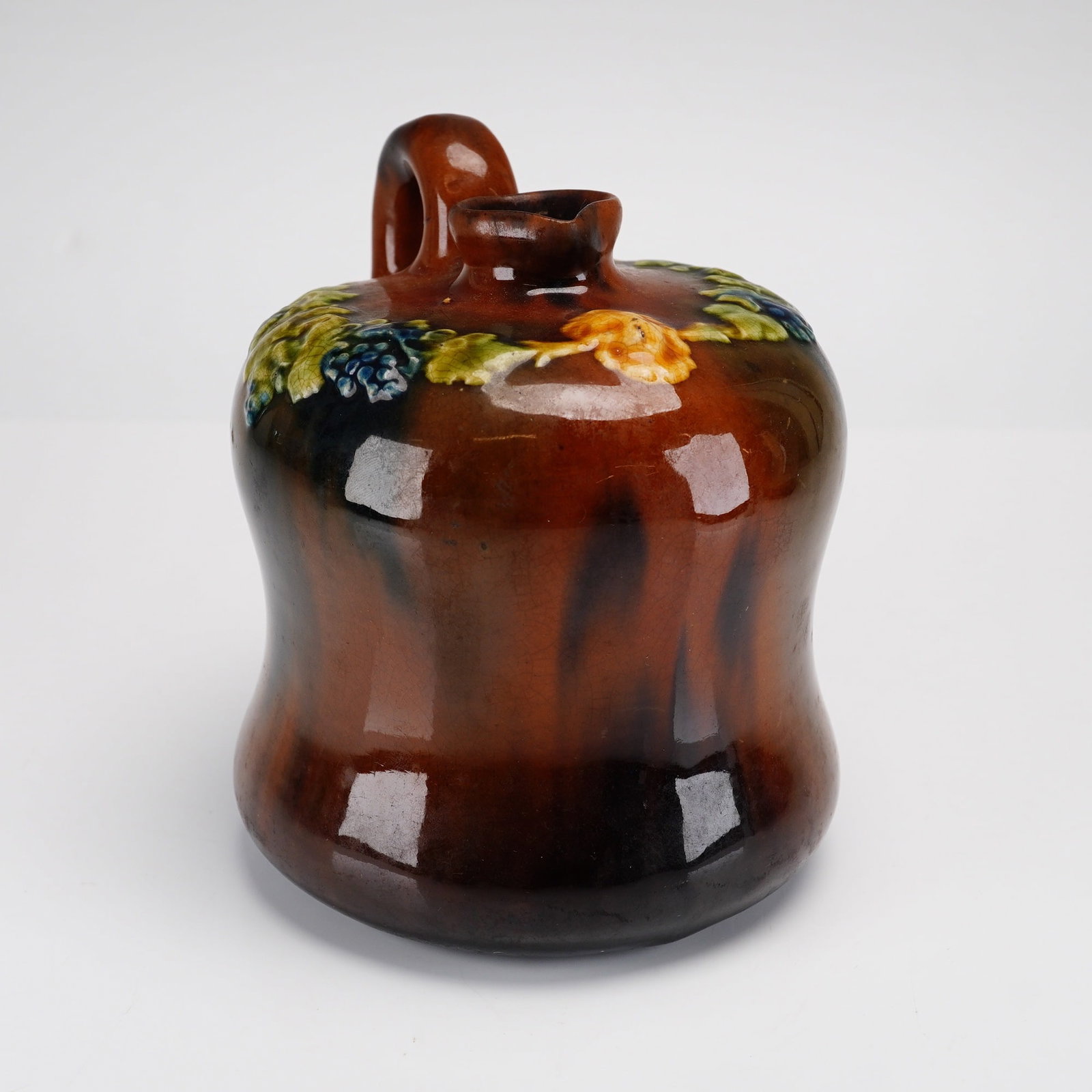 Peters and Reed Pottery Standard Glaze Relief-Molded Grape Jug: This small earthenware jug was produced by Peters and Reed Pottery of Zanesville, Ohio, during the early 20th century. The vessel features a squat, bulbous body with a slightly flared base, a short ne