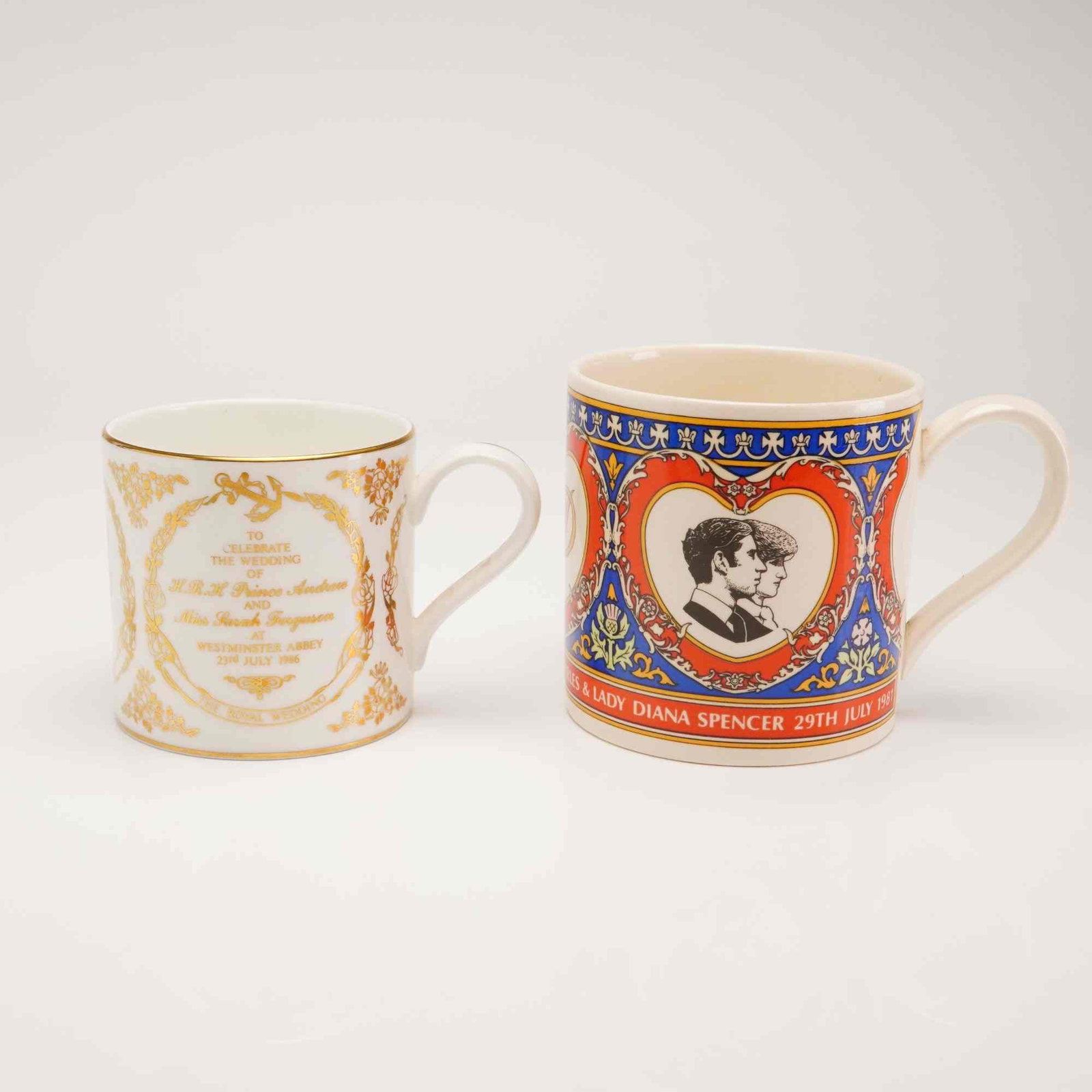 2pc Wedgwood British Royal Family Commemorative Wedding Cups: A pair of commemorative cups manufactured by Wedgwood to celebrate British royal weddings. The smaller cup is made of white bone china and features gold-tone decorative scrollwork with text commemorat