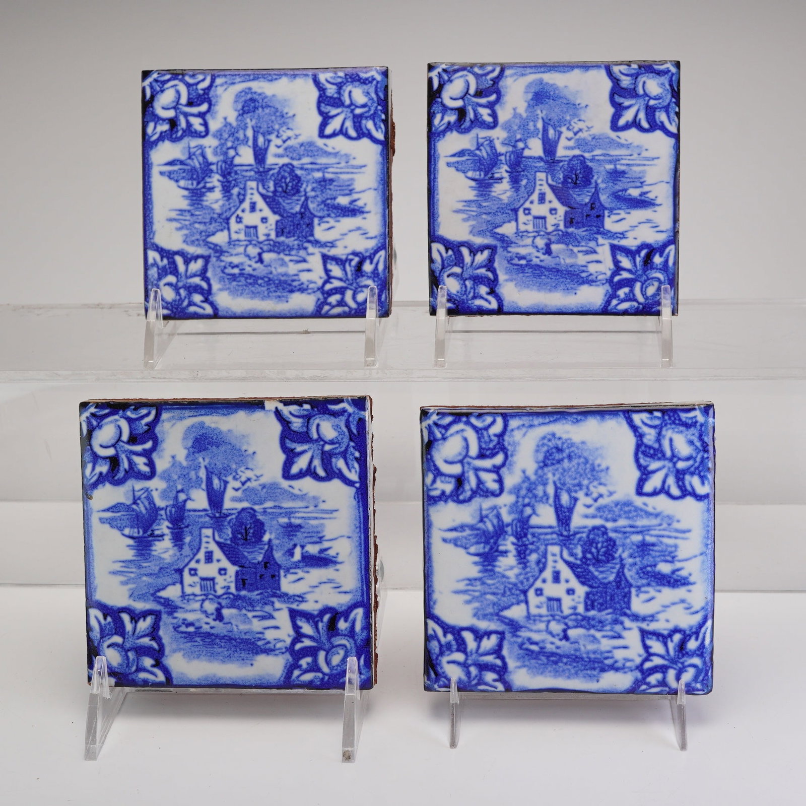 Mosaic Tile Co. Delft-inspired Seaside Cottage Faience Tiles: A set of four faience tiles produced by the Mosaic Tile Co. featuring a Delft-inspired seaside cottage pattern. Each tile is constructed from a red earthenware body decorated with a monochromatic blue