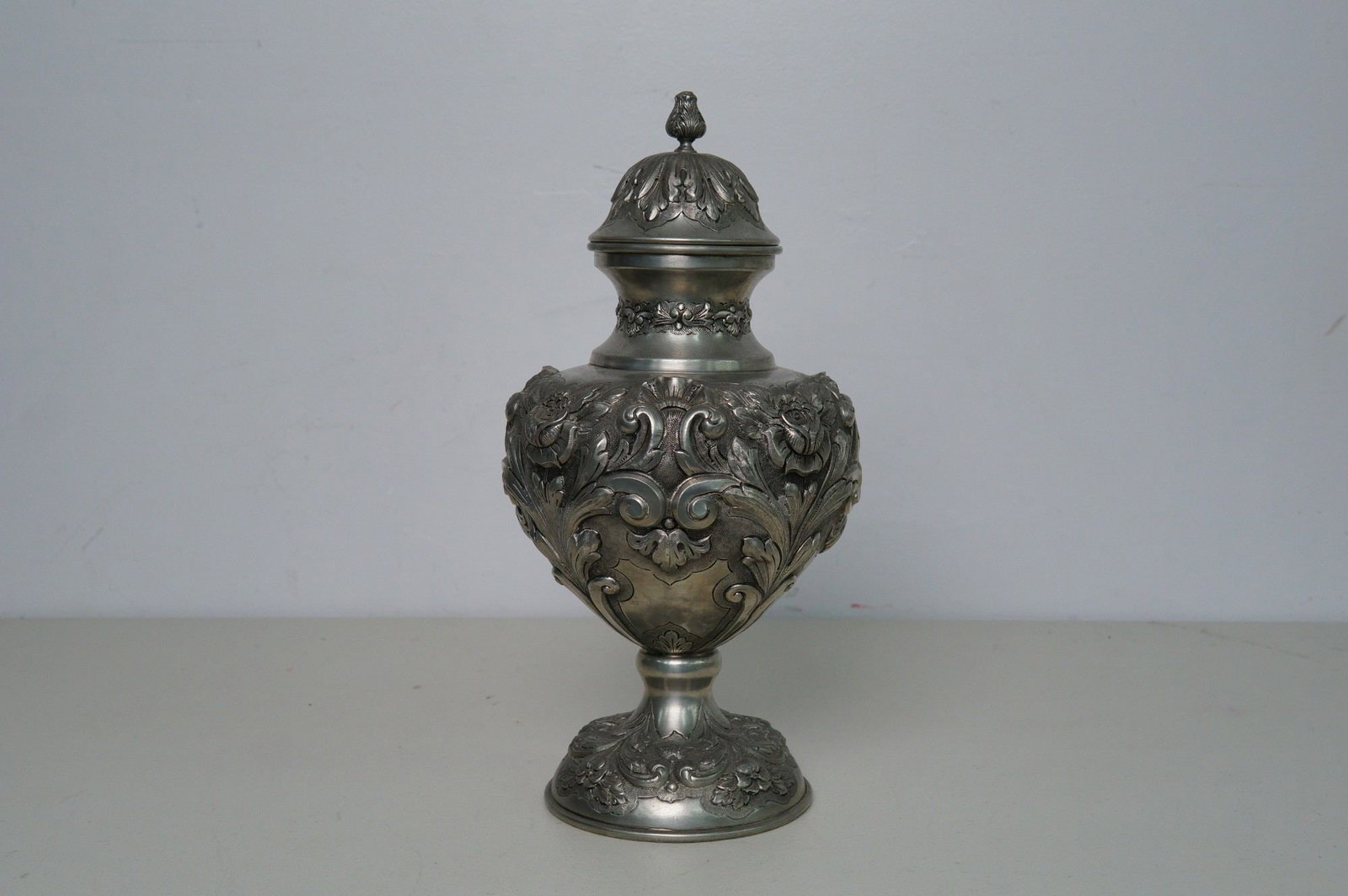 J. Dores Estanhos Embossed Pewter Lidded Urn: Mid-century pewter decor piece made in Portugal. Designed with elaborate floral reliefs, acanthus leaf scrolling and an ornamental finial. J Dores Estanhos impressed mark on base with foil label Made 