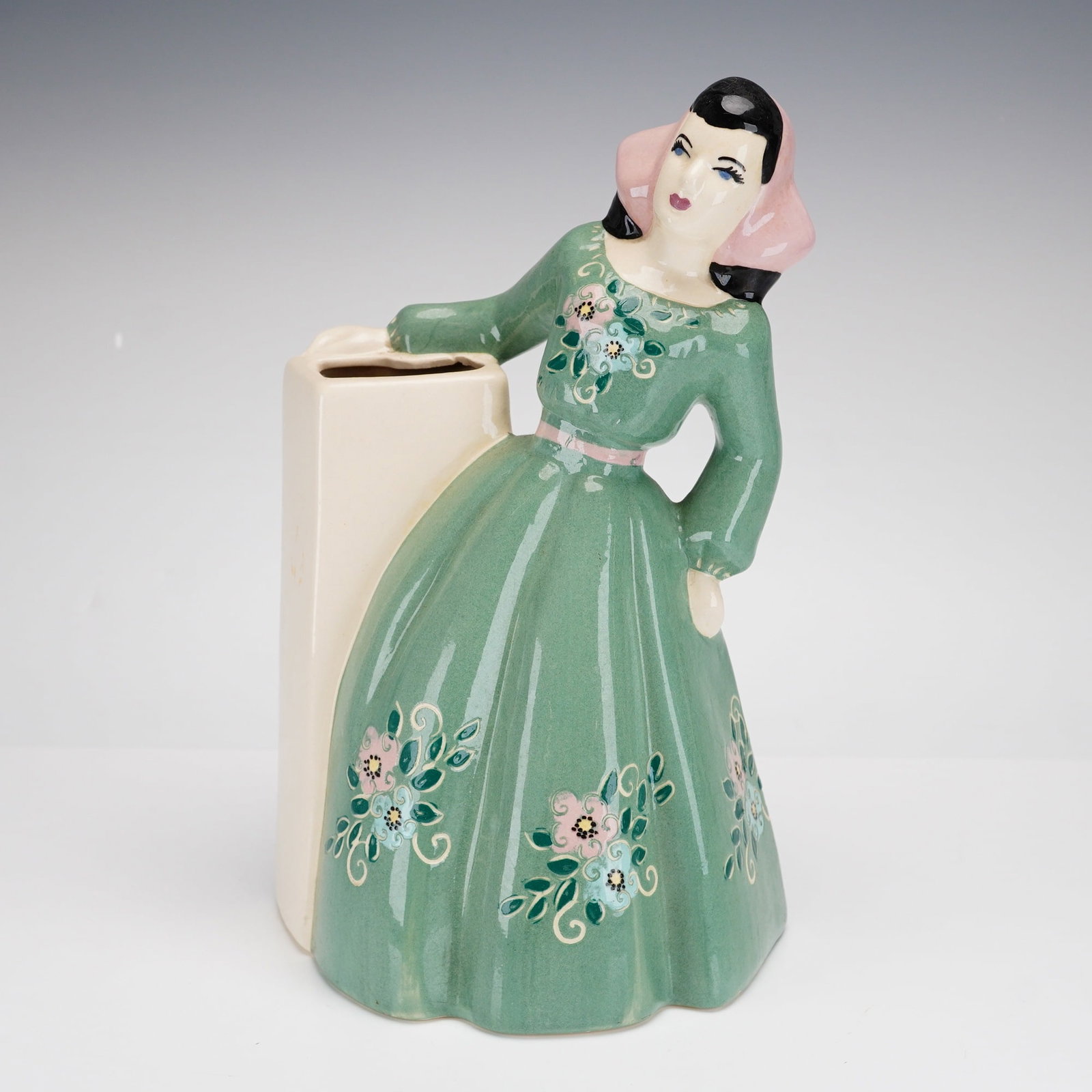 Weil Ware, Figural Lady Vase Model 4052: A mid-century modern glazed ceramic figural vase produced by Weil Ware of California. This piece, model number 4052, depicts a woman in a stylized floor-length green gown with a pink sash and bonnet, 