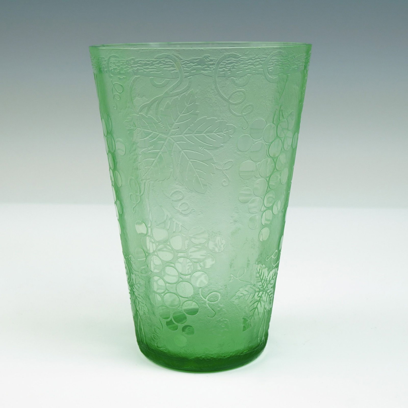Green Pressed Glass Tumbler with Grape and Vine Decoration: A vibrant green pressed glass tumbler decorated in relief with a pattern of grape clusters, tendrils, and large vine leaves. The matte-textured ground contrasts subtly with the glossy raised design, g