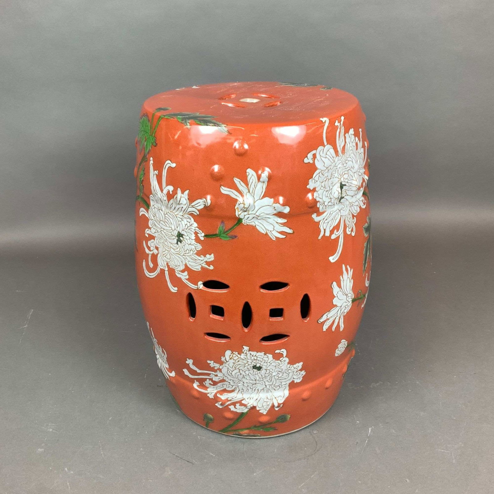 Gump's San Francisco Hand-Painted Chinese Porcelain Garden Stool: This barrel-shaped porcelain garden stool features a vibrant coral-orange ground decorated with hand-painted white chrysanthemum blossoms on leafy green stems. The exterior is accented with rows of ra