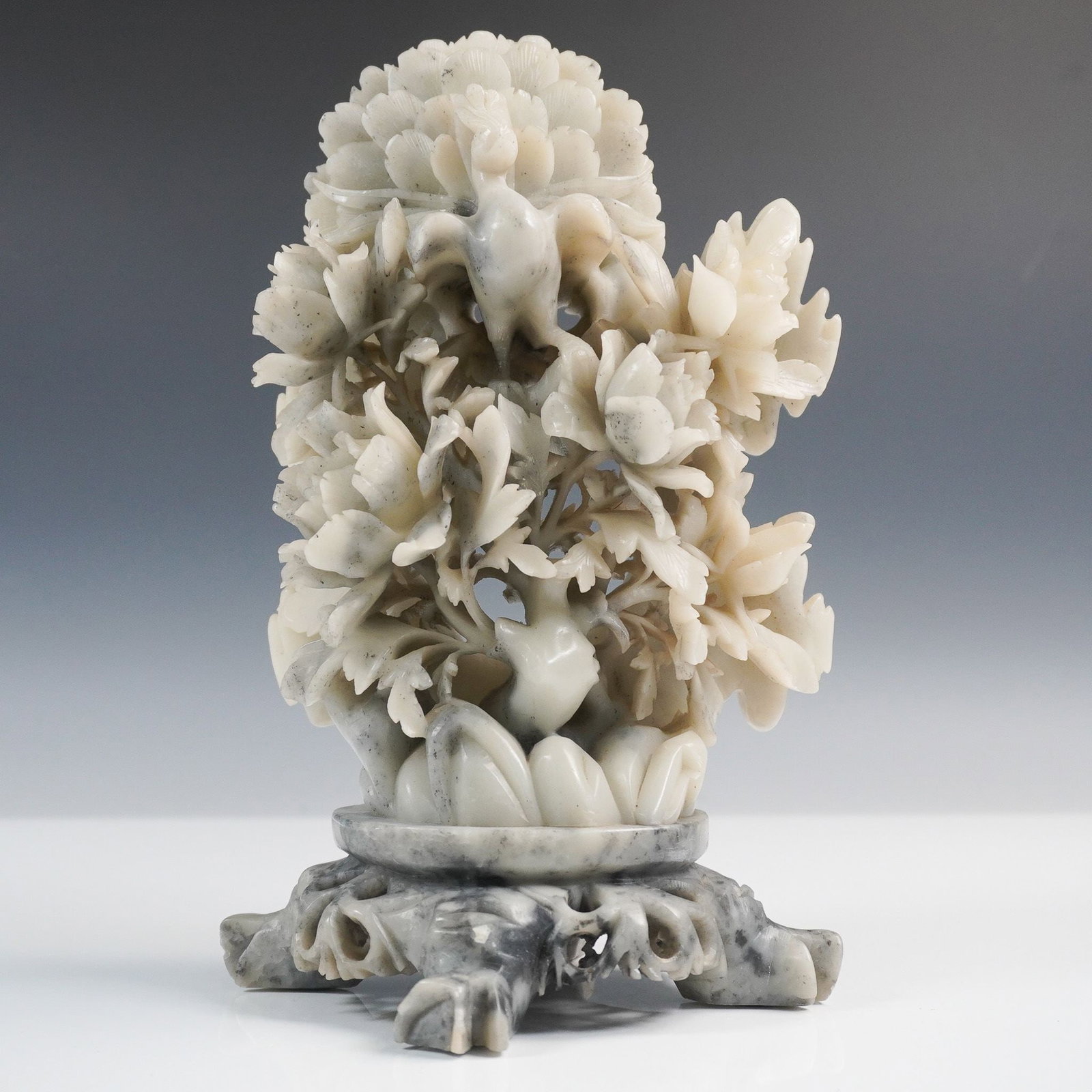 Chinese Soapstone Carving of Peacock and Peonies: An intricately carved Chinese soapstone sculpture depicting a regal peacock perched among blooming peony flowers. The peacock, a traditional Chinese symbol of beauty and prosperity, is shown with a fu