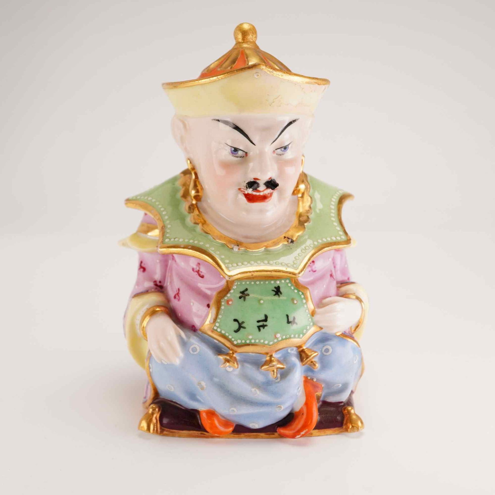 Chinoiserie Lidded Porcelain Seated Chinese Man Figure: A polychrome enameled and gilded porcelain lidded jar, modeled in the Chinoiserie style. The vessel depicts a seated male figure in Orientalist attire, featuring a conical hat with a gilded finial, a 
