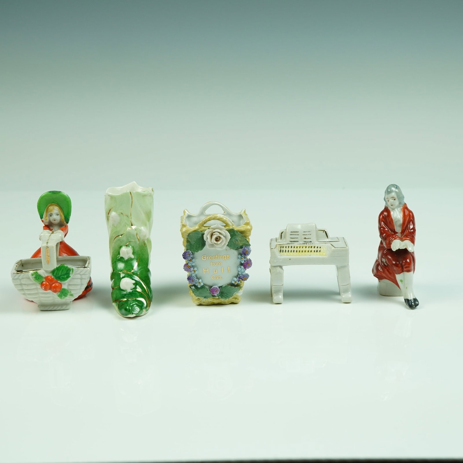 Porcelain Miniatures w/ Hull Canada Basket & Piano w/ Gentleman: An enchanting collection of five porcelain miniatures, this lot includes a variety of charming, hand-painted ceramic figures with delightful character. Highlights include a souvenir floral basket mark