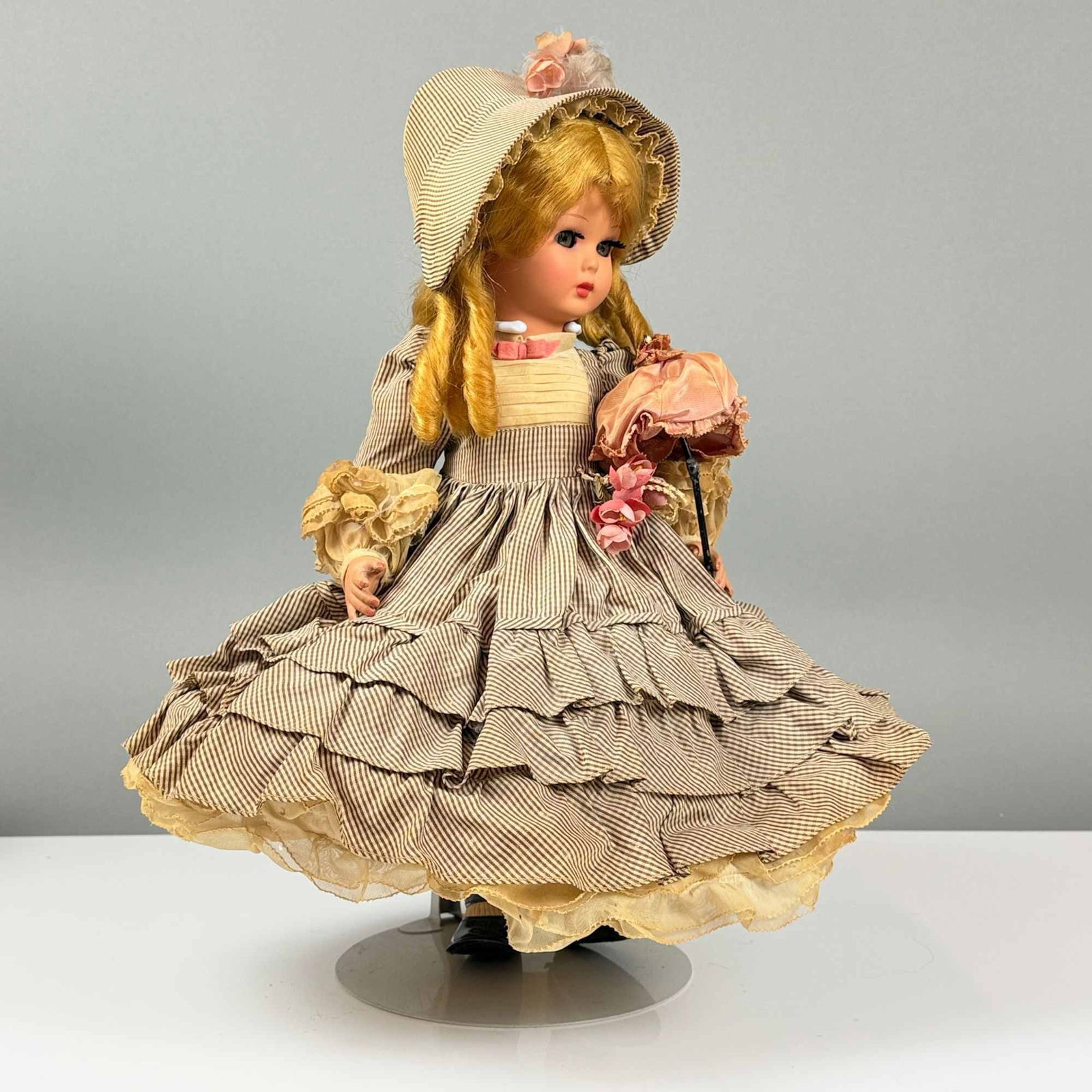 L. Furga and C. Italian Collector Doll with Hat and Parasol: This mid-20th-century collector doll is an L. Furga and C. Italian model. The doll features a vinyl head with golden blonde hair styled in ringlets, blue sleep eyes with lashes, and painted facial fea