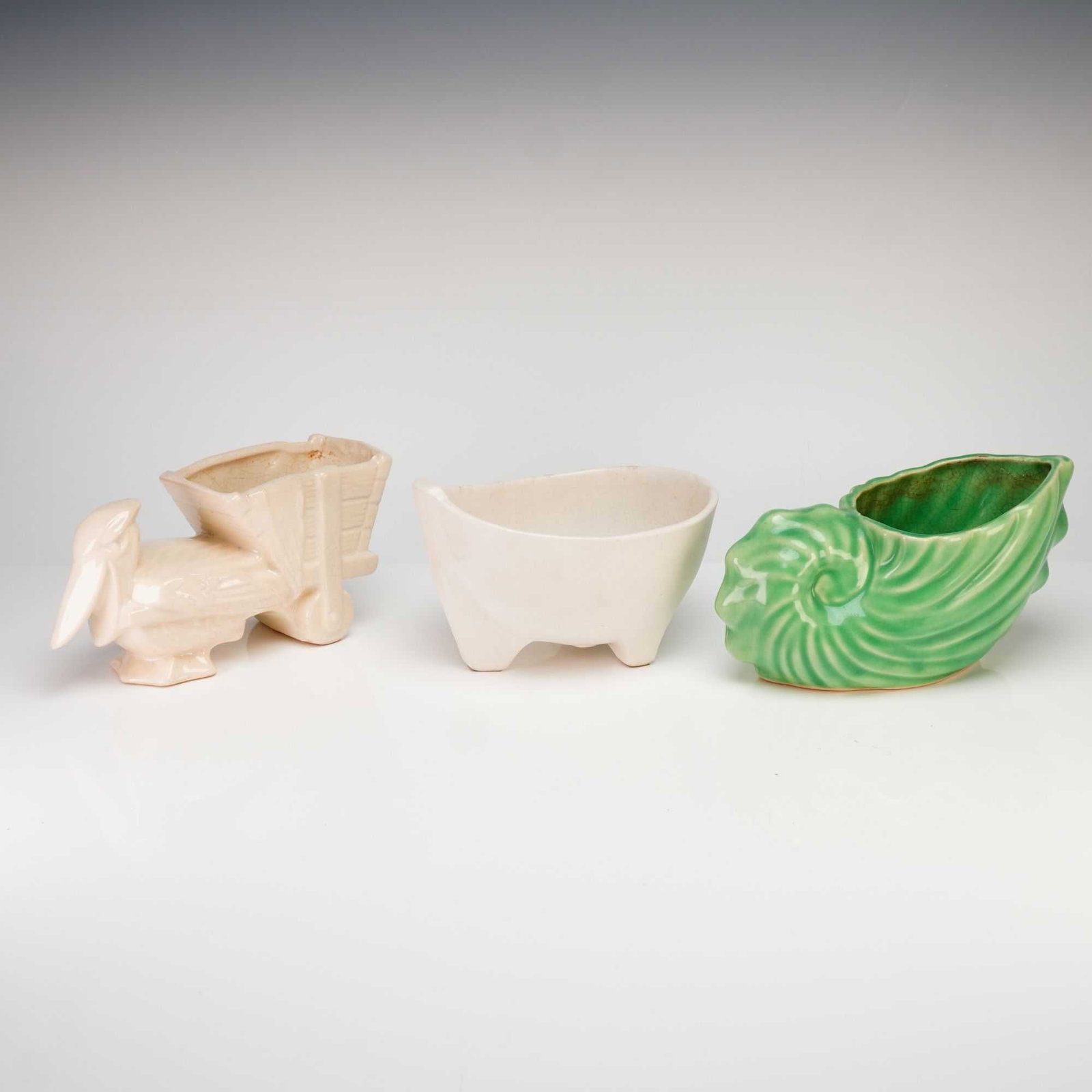 Three McCoy Pottery Glazed Ceramic Planters and Green Shell Planter: A collection of three vintage McCoy Pottery glazed ceramic planters featuring distinct mid-century forms. The group includes a green nautilus shell-shaped vessel with a ribbed texture, a cream-colored