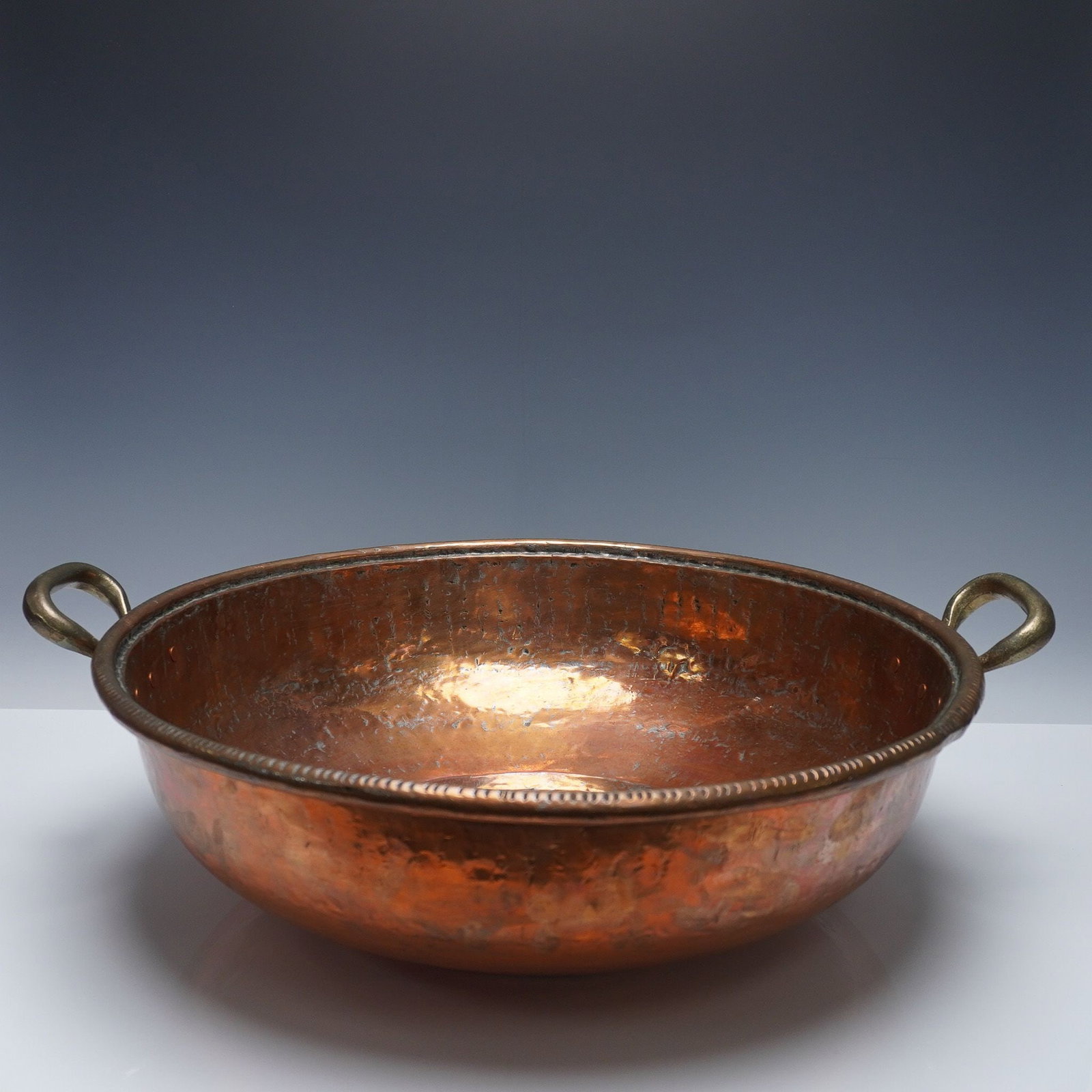 Large Hand Hammered Copper Bowl with Brass Handles: A substantial and beautifully hand crafted hammered copper bowl with twin brass handles. This generously scaled vessel features a wide, shallow form with raised rounded base and a delicately beaded ri