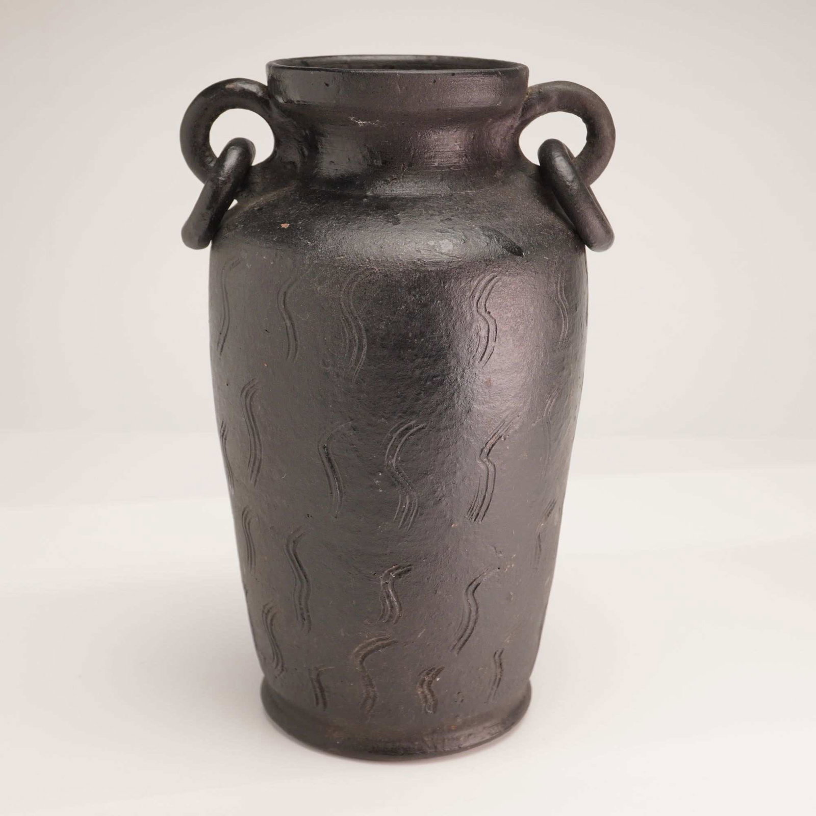 Ceramic Ring-Handled Jar in Gunmetal Black: A stoneware vessel featuring a tapered, ovoid body that narrows toward a flat base and widens at the shoulder. The piece is finished in a matte gunmetal black, achieved through a blackened slip or red