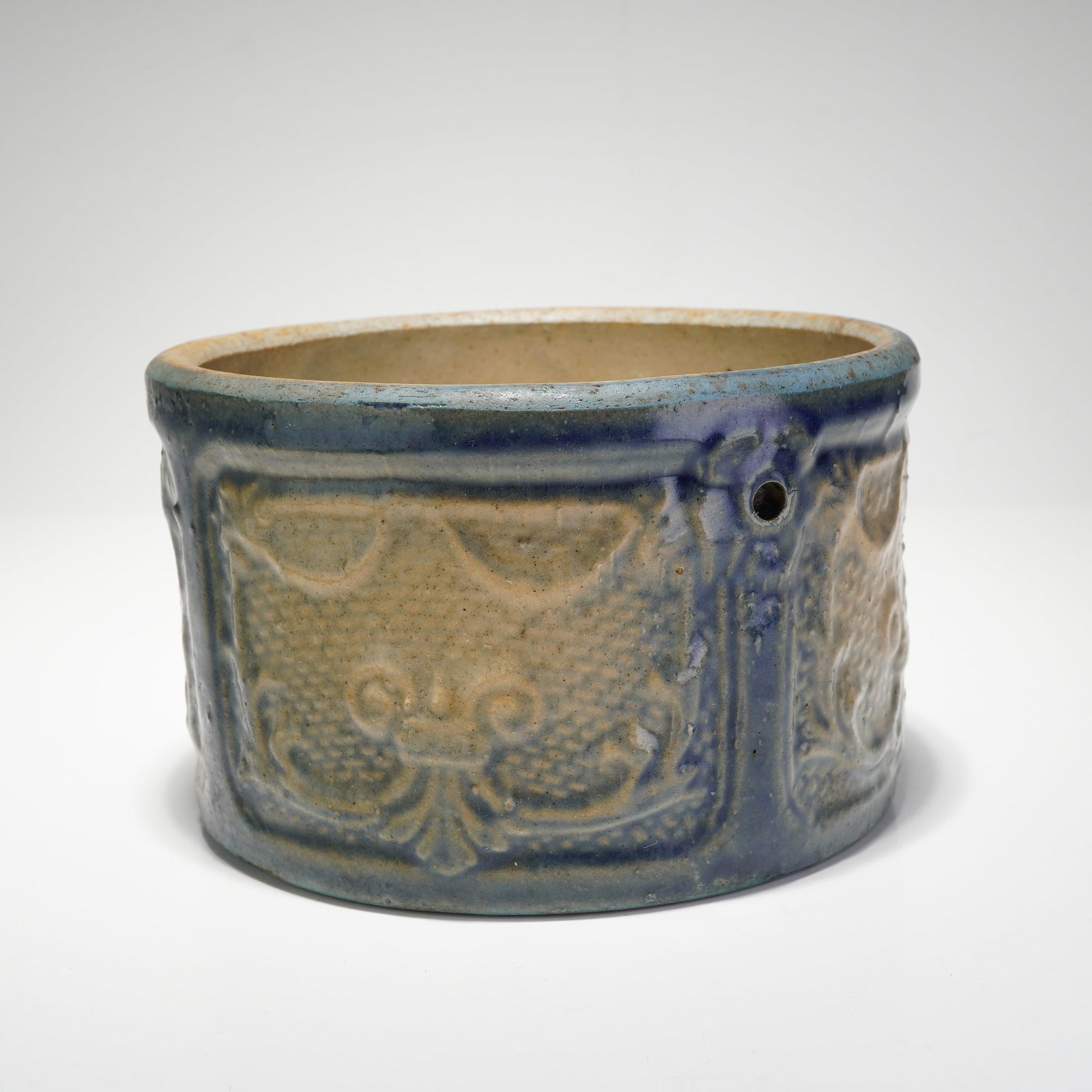 Antique Cobalt Blue Salt-Glaze Embossed Pattern Stoneware Butter Crock: This antique stoneware butter crock features blue salt-glaze embossed patterns and a cylindrical form. The exterior is decorated with three molded relief panels containing stylized symmetrical floral 